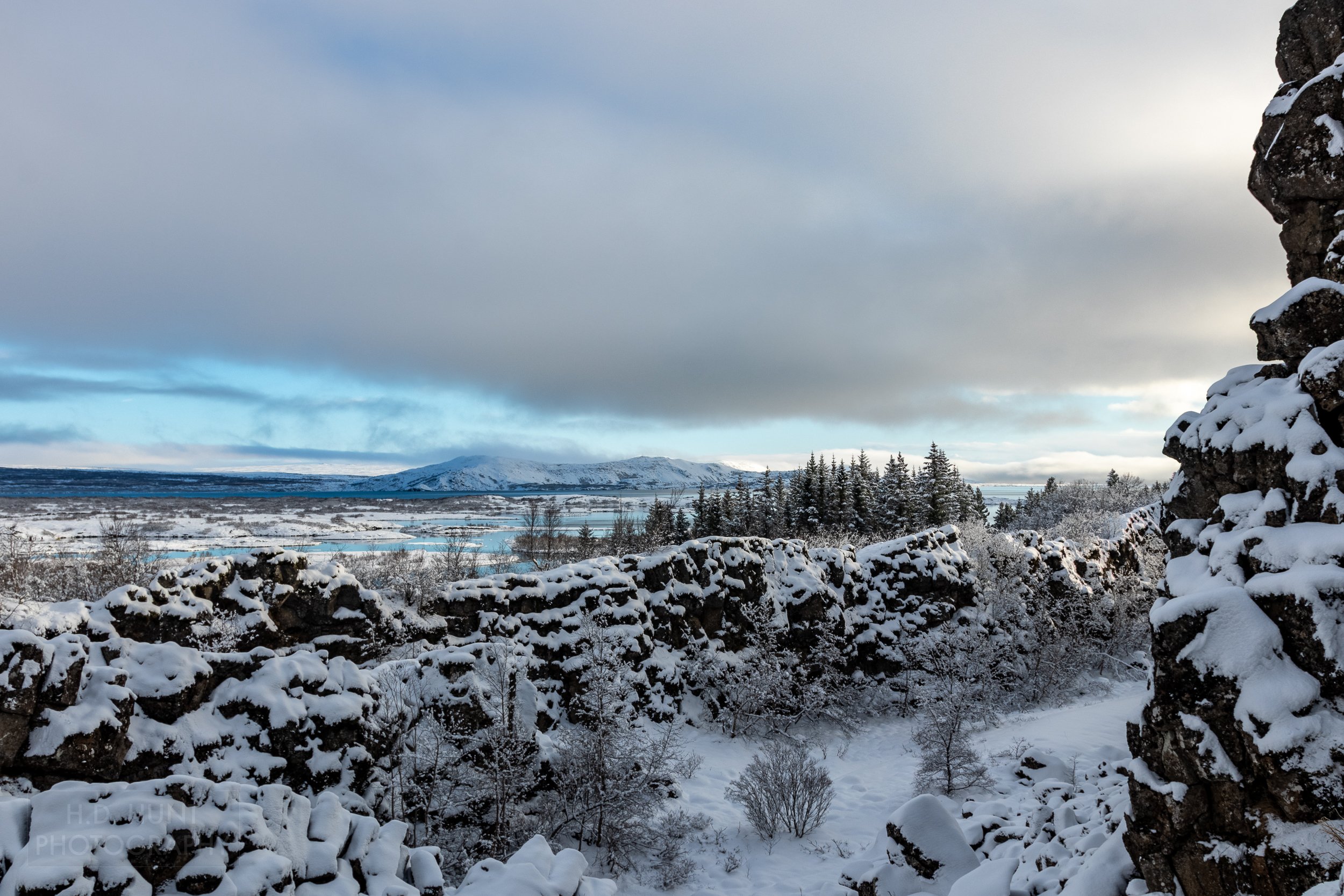A snow-covered stone wall obscures views of a lake at Þingvellir, Iceland.