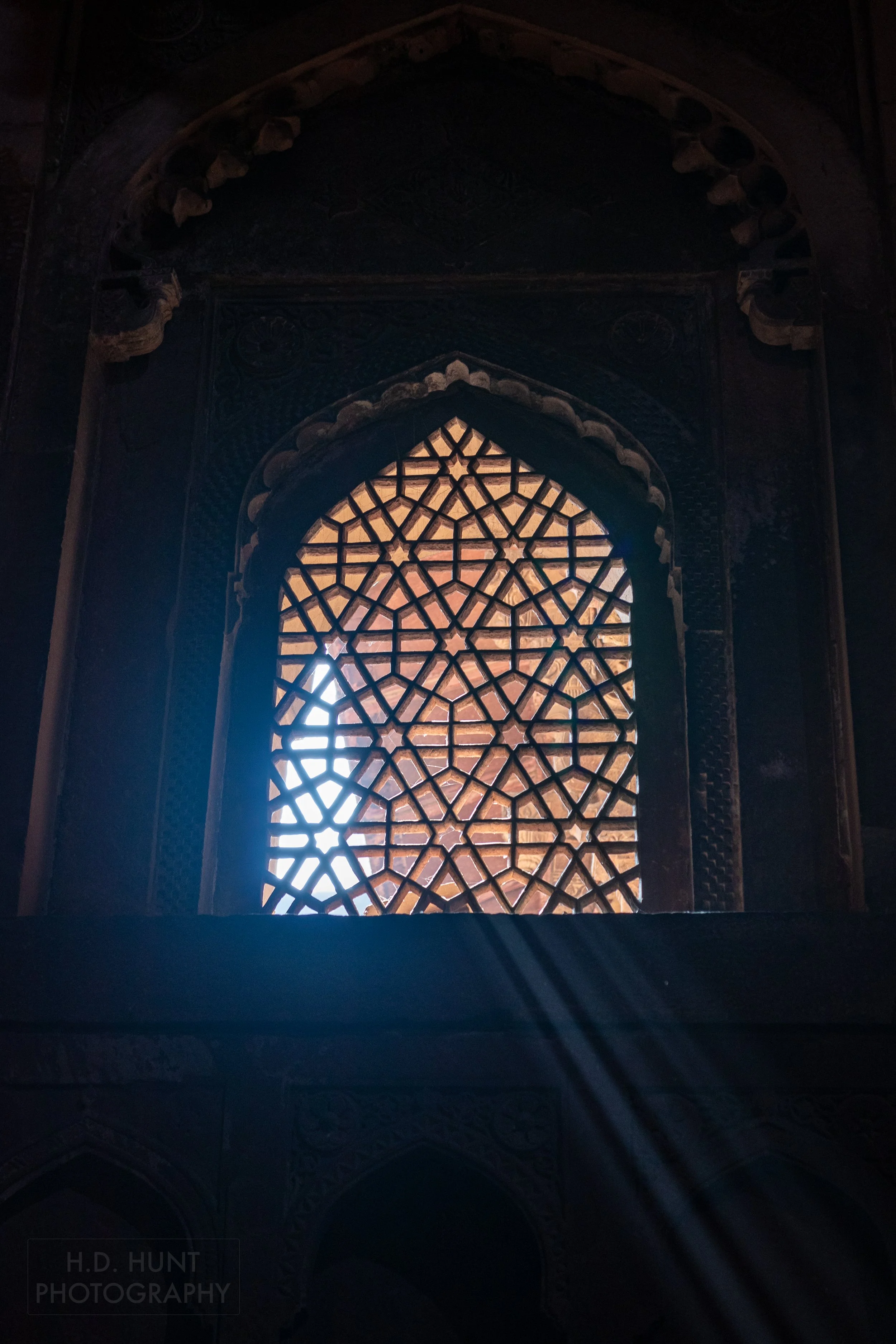 A beam of light passes through an intricately carved stone window screen, Agra Fort, Agra, India.