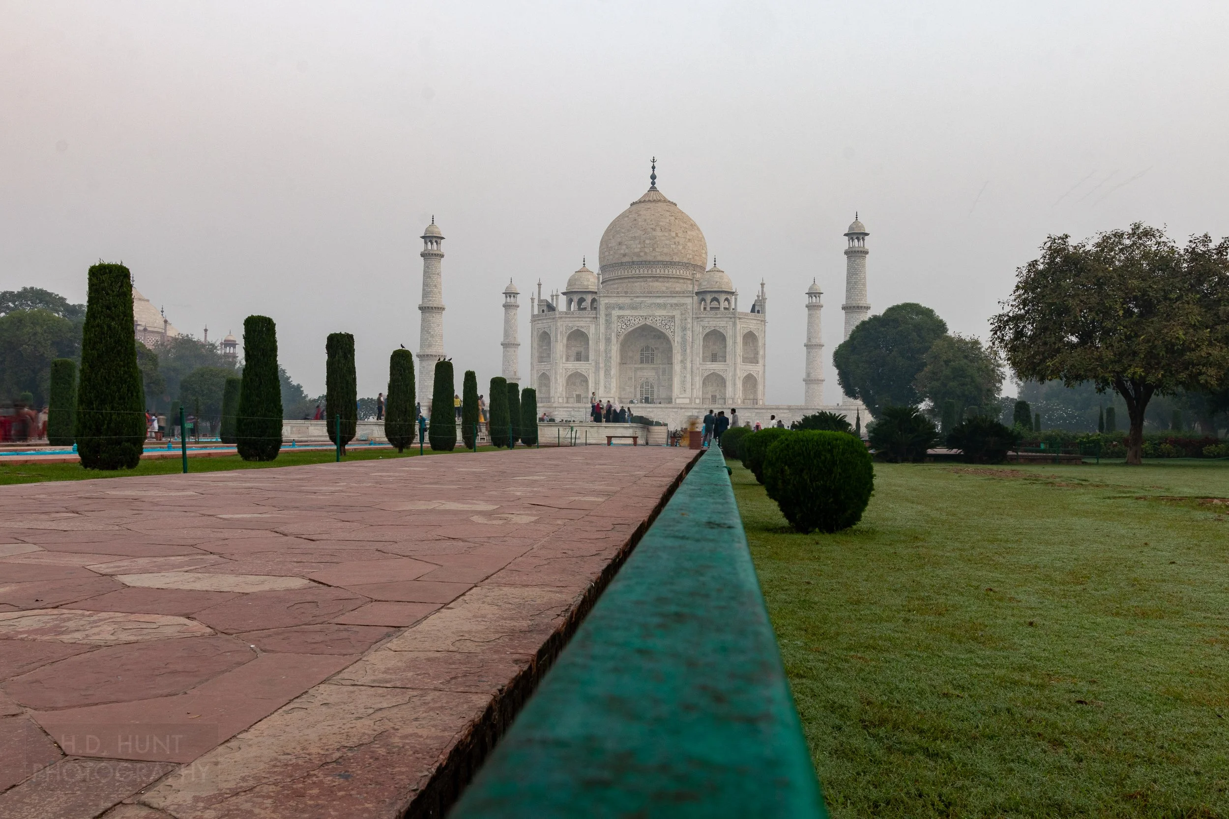 A red brick walkway next to manicured grass leads to the main mausoleum building of Taj Mahal, Agra, India.