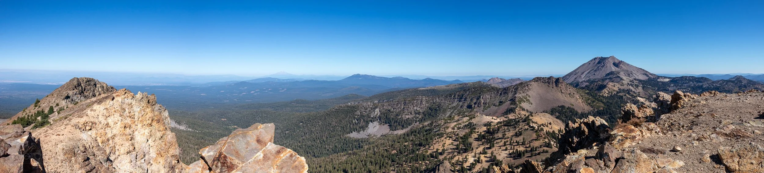 A panorama from atop Brokeoff Mountain, Lassen Volcanic National Park, California, United States, showing Lassen Peak near the foreground and Mount Shasta far in the background.