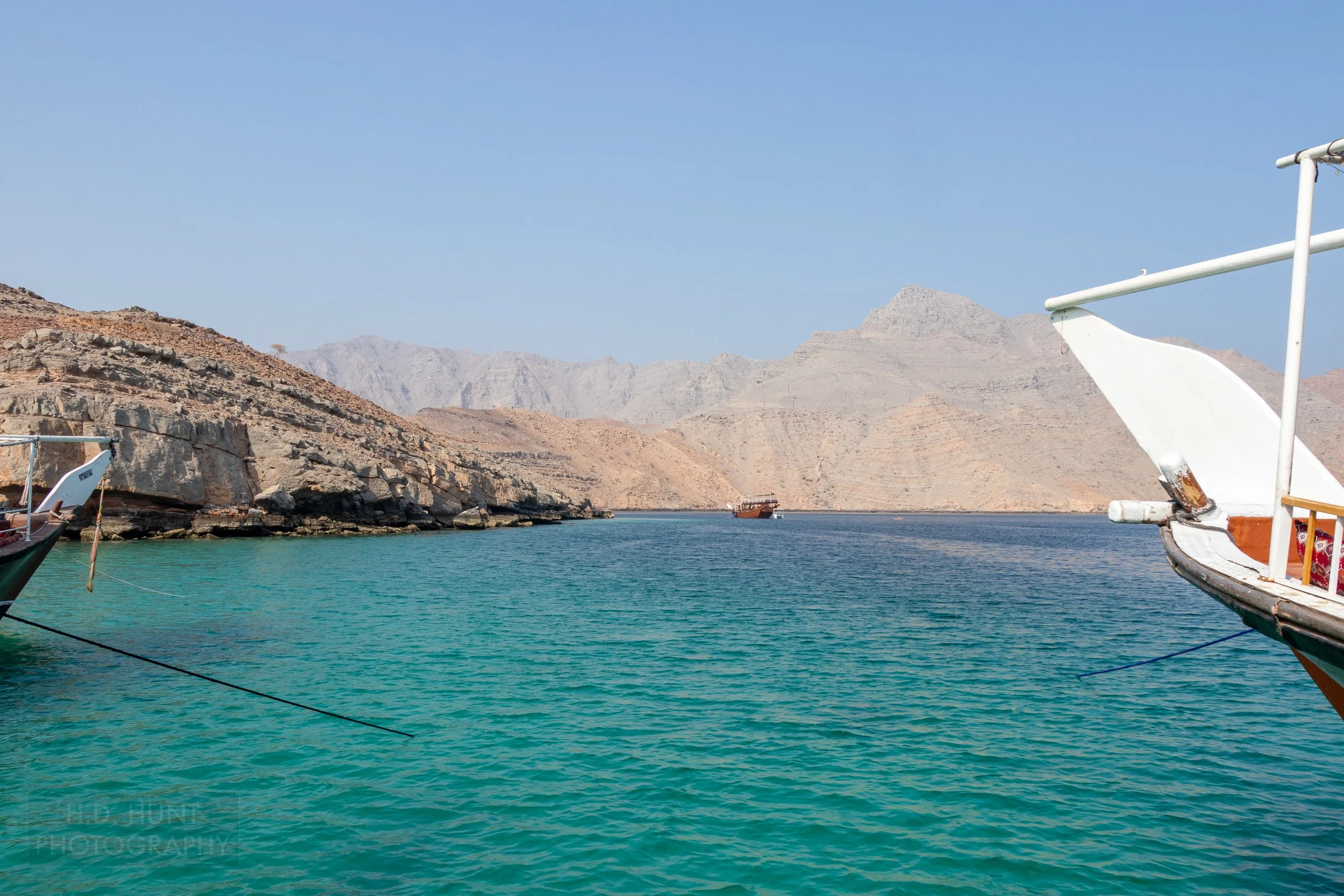 Two dhow boats' anchor lines are seen submerging into the green-blue waters off the Musandam Peninsula, Oman.