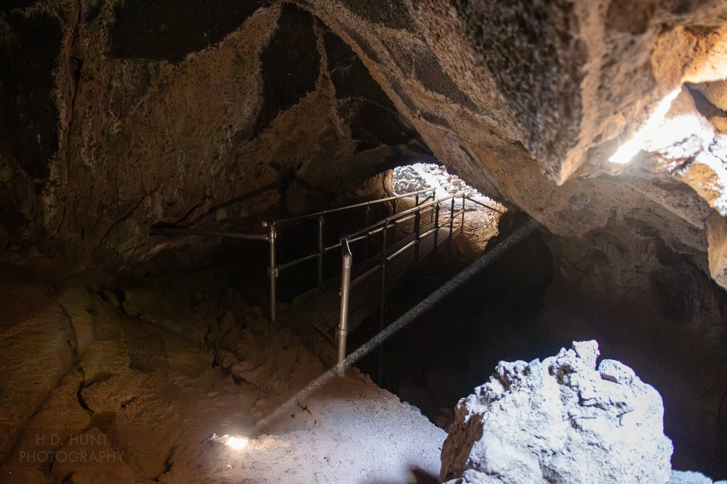 A beam of light penetrates the ceiling of a lava tube, illuminating the tunnel's floor, Lava Beds National Monument, California, United States.