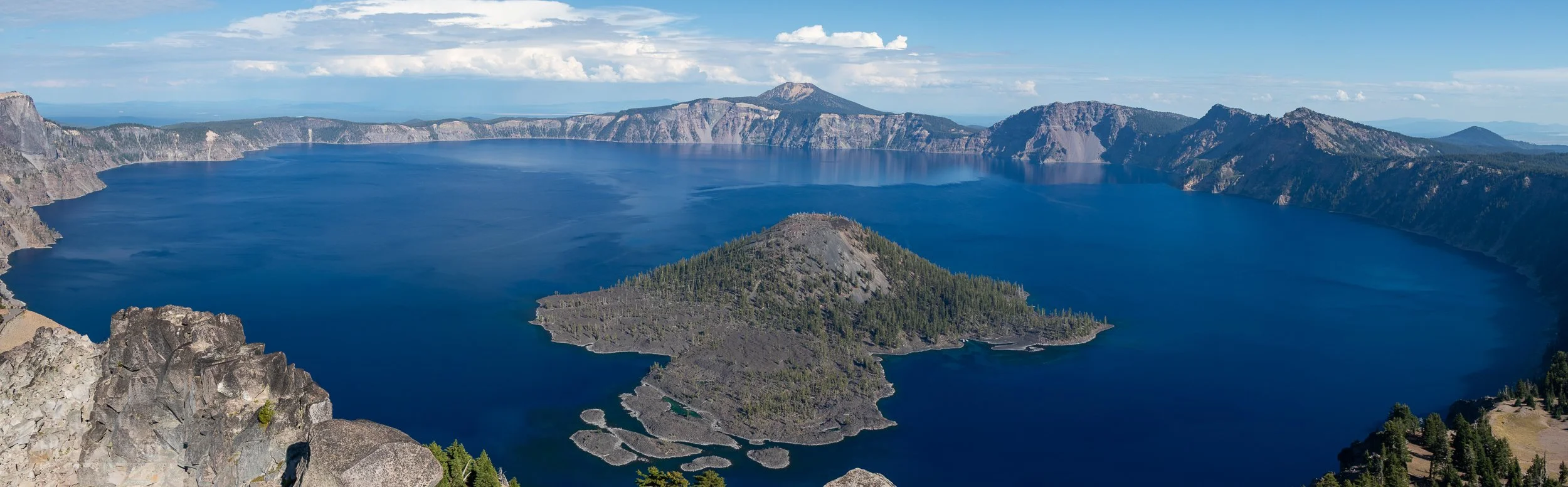 A panorama of the blue waters of Crater Lake with Wizard Island featured prominently in the foreground, Crater Lake National Park, Oregon, United States.