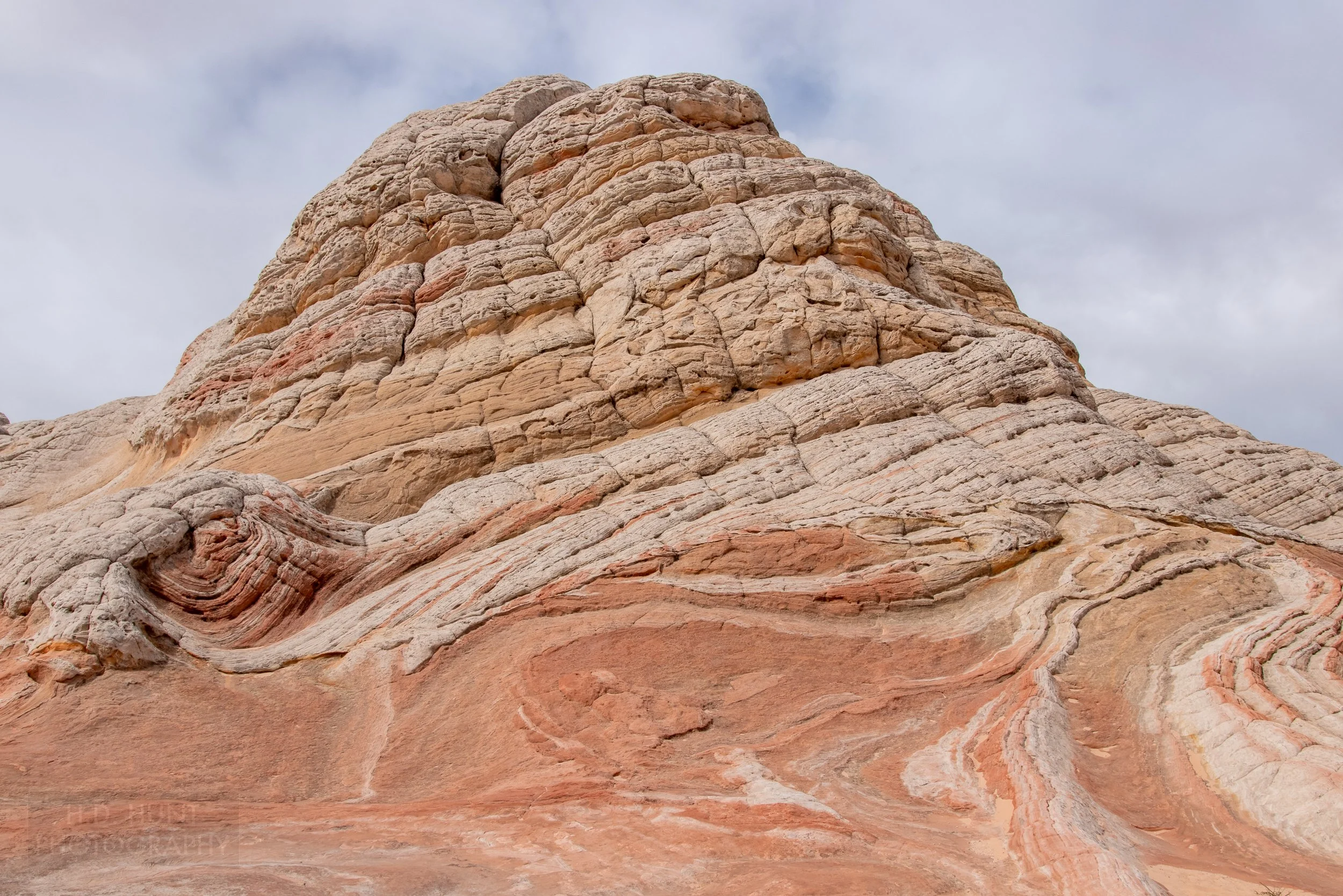 A heavily deformed striped white and tan rock  mound sits above a bedrock of red sandstone, White Pocket, Vermillion Cliffs National Monument, Arizona, United States.