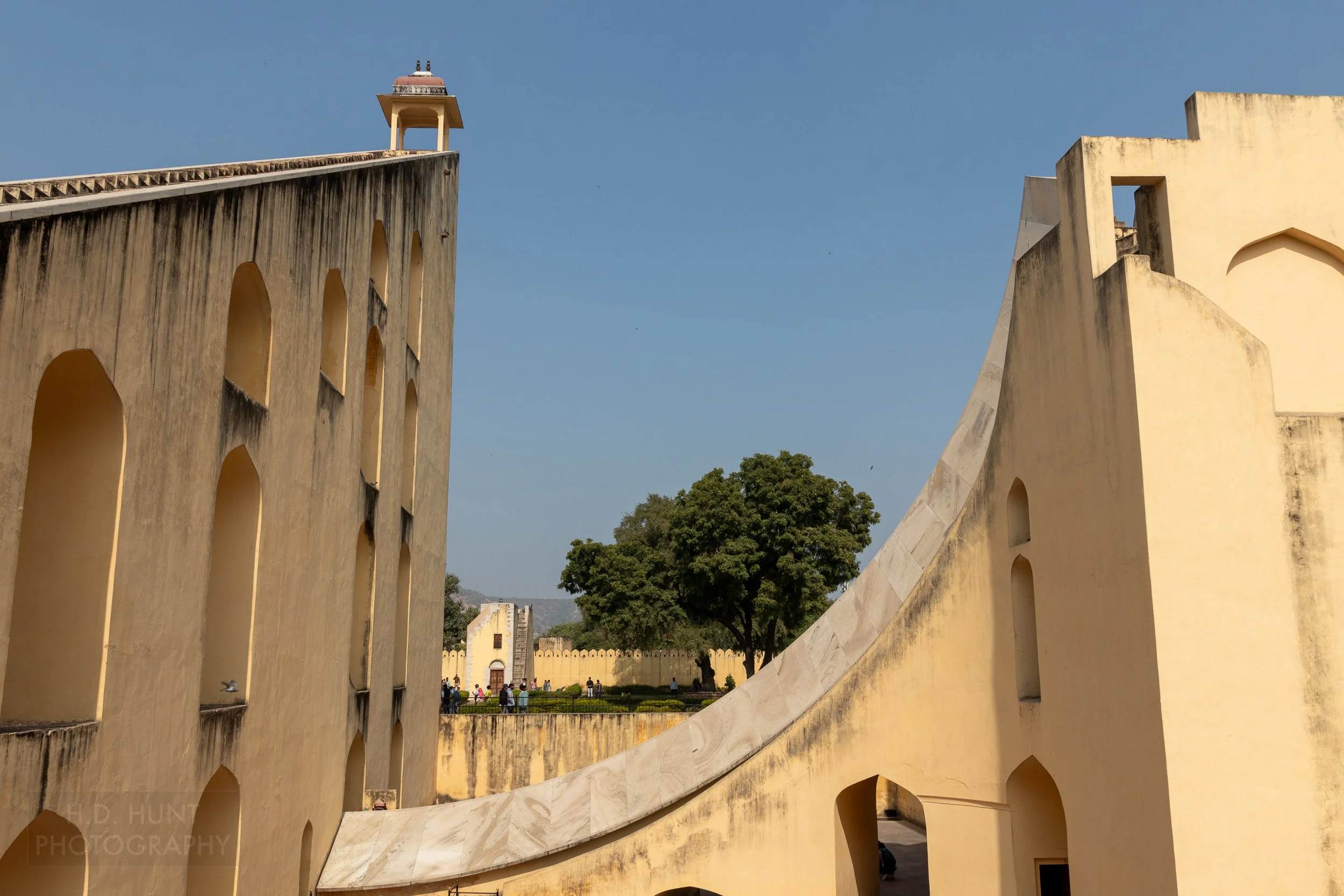 A large stone arc rises beside a large stone staircase forming a large sundial, Jantar Mantar, Jaipur, India.