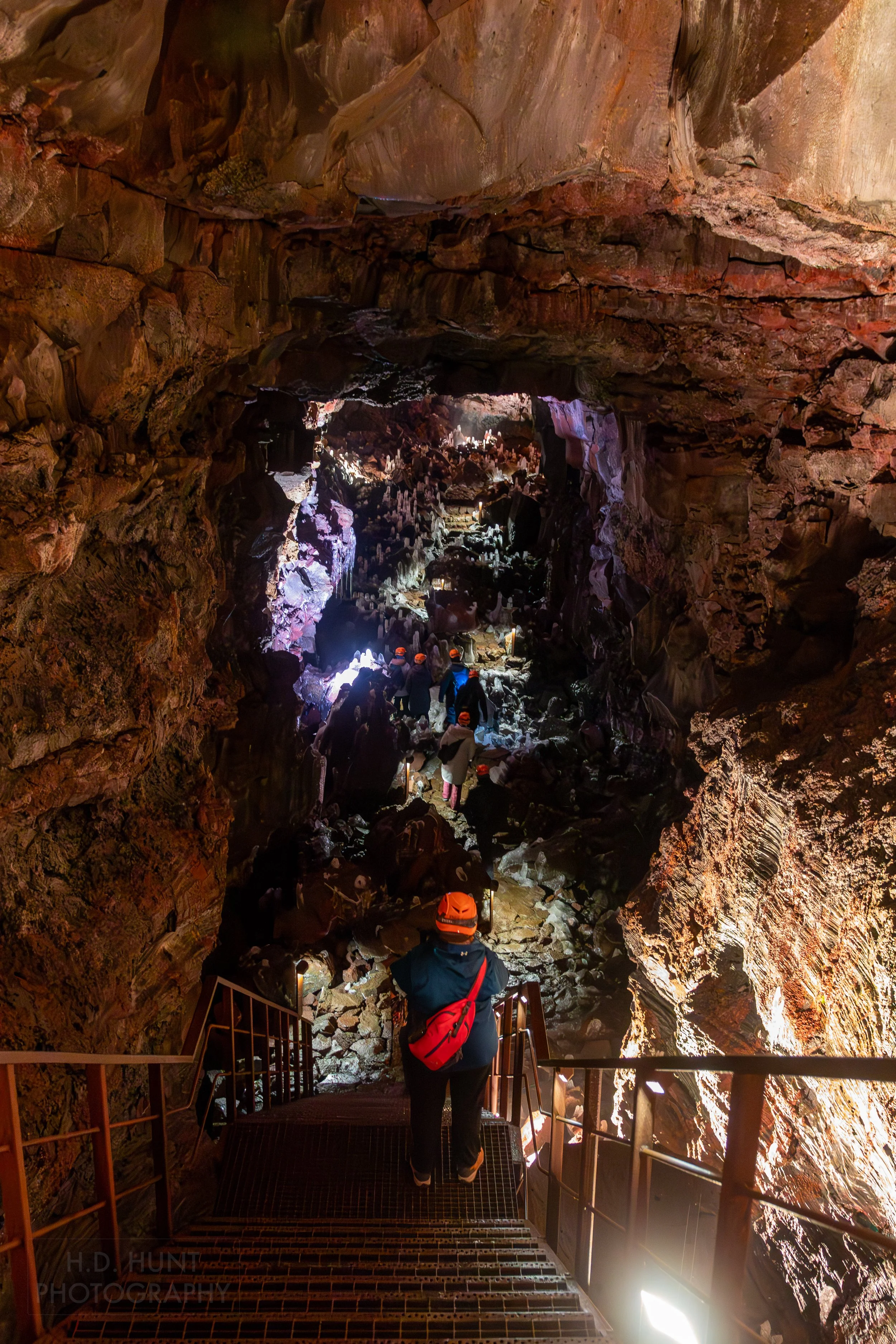 Visitors walk through a rocky passage with high stone ceilings within the lava tube Raufarhólshellir, Iceland.