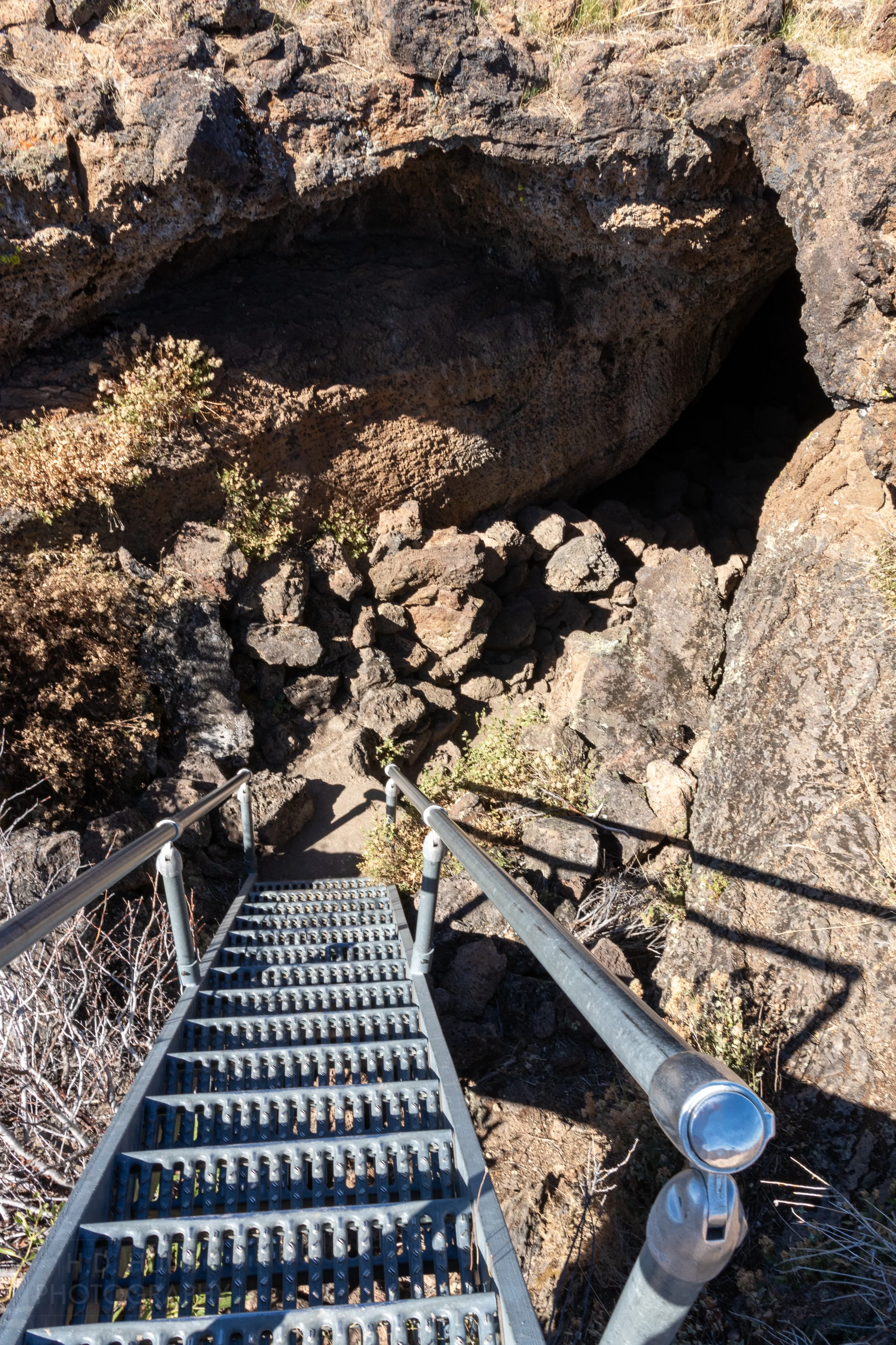 A steep metal staircase drops into a large cave opening, Lava Beds National Monument, California, United States.
