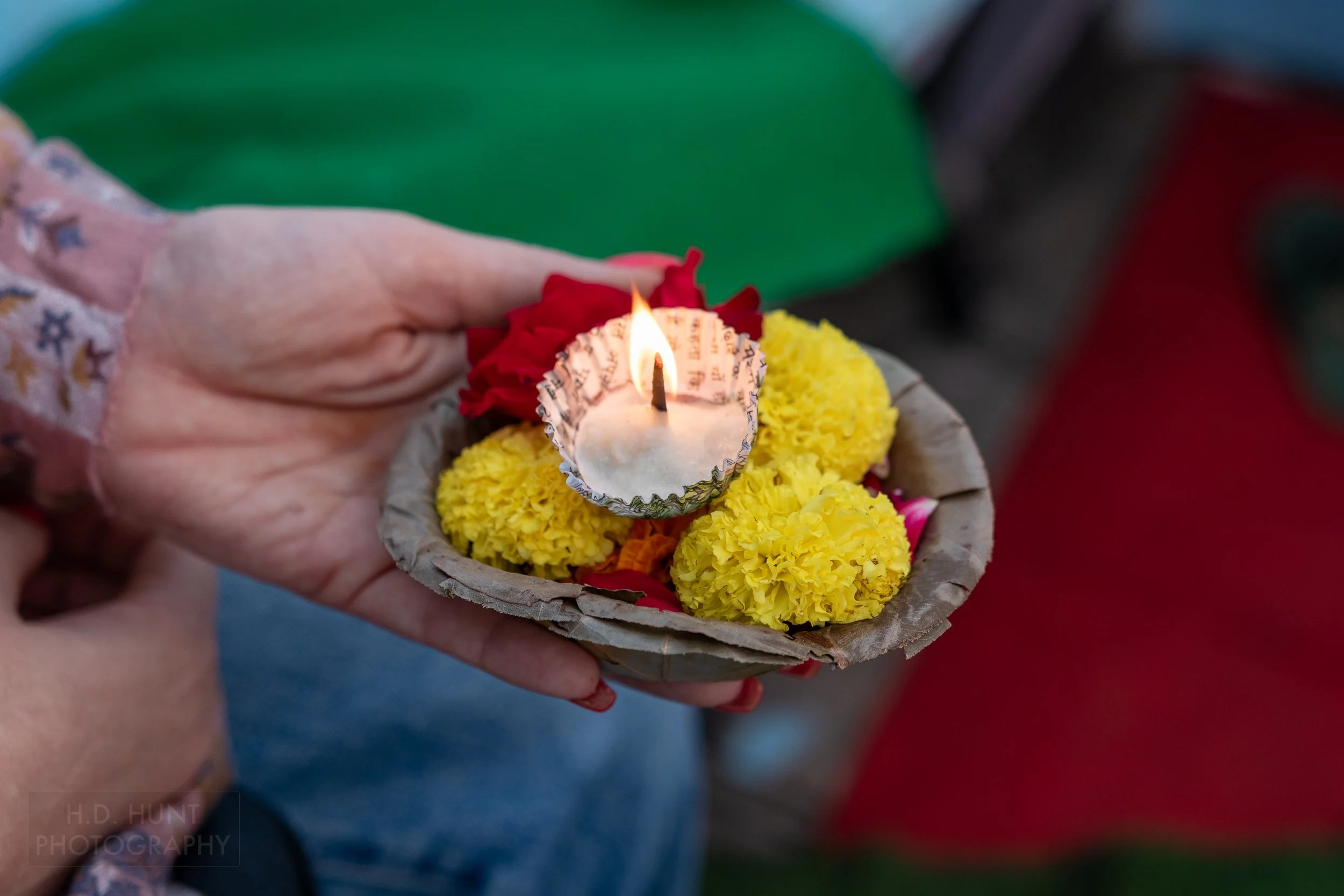 A small white candle surrounded by yellow and red flowers being held, Varanasi, India.