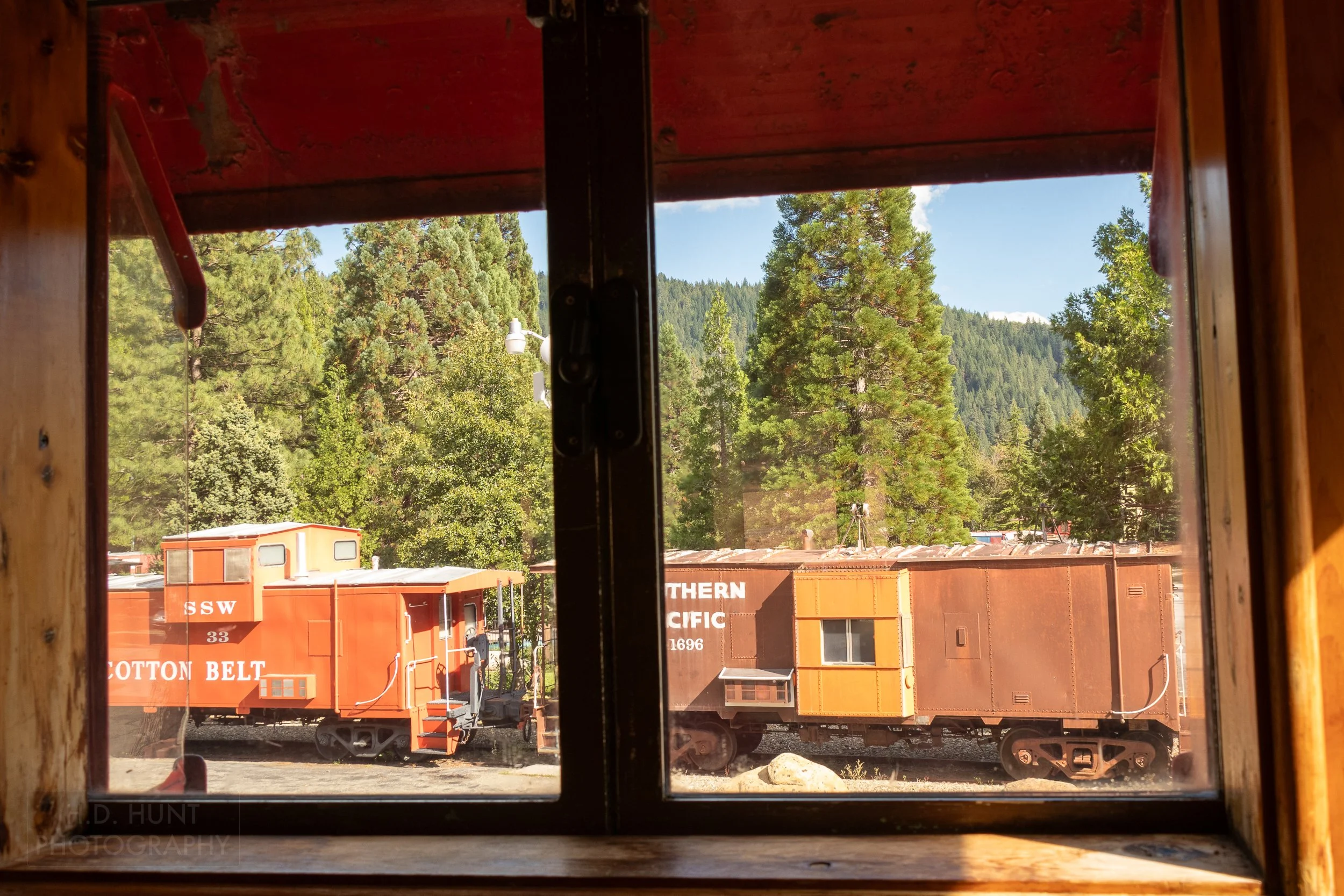 Two railroad cars are seen outside the window of a third surrounded by pine trees at the Jubilee Railroad Wilderness Lodge, Dunsmuir, California, United States.