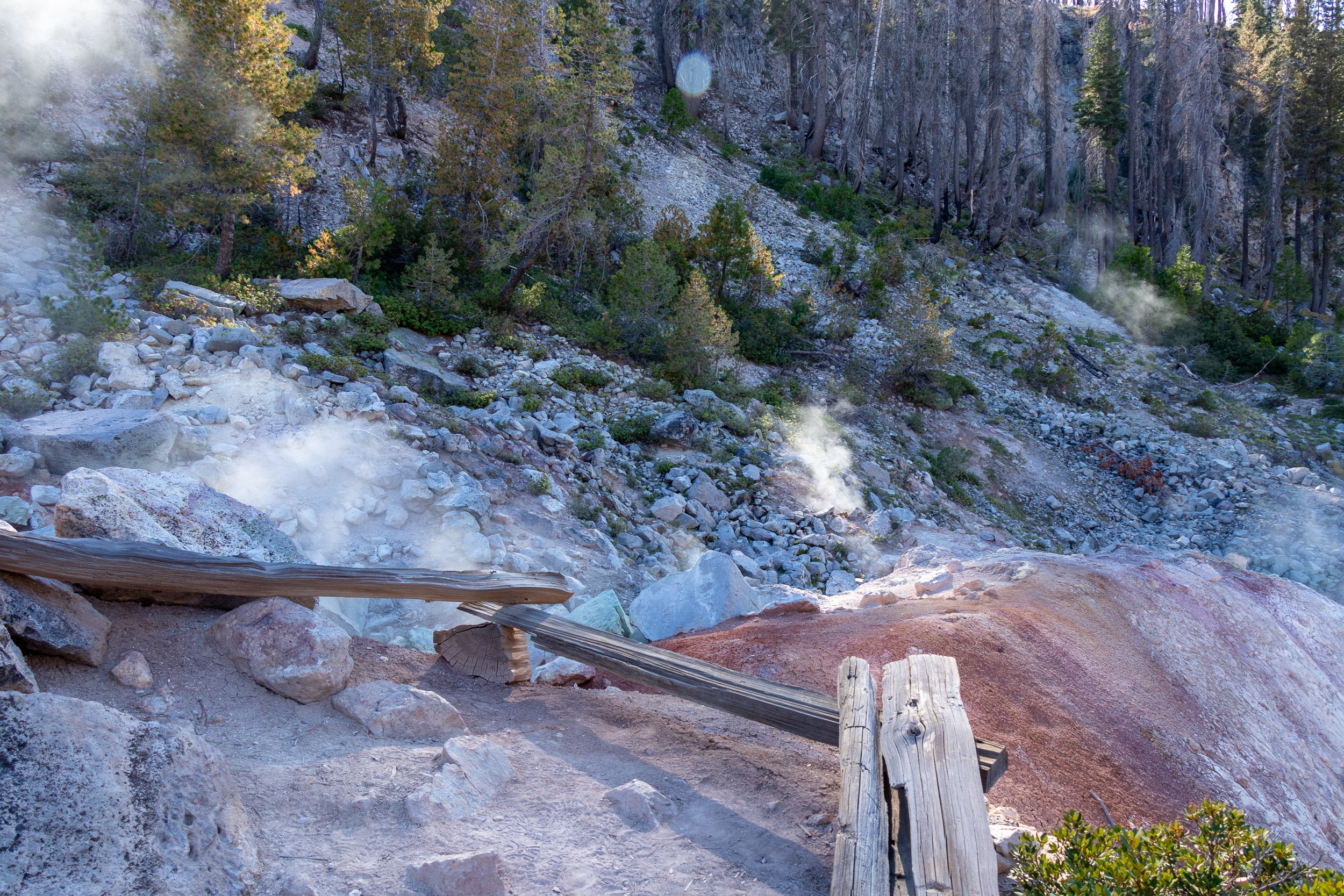 Steam rises from white and red rock cordoned off by a wooden fence, Lassen Volcanic National Park, California, United States.