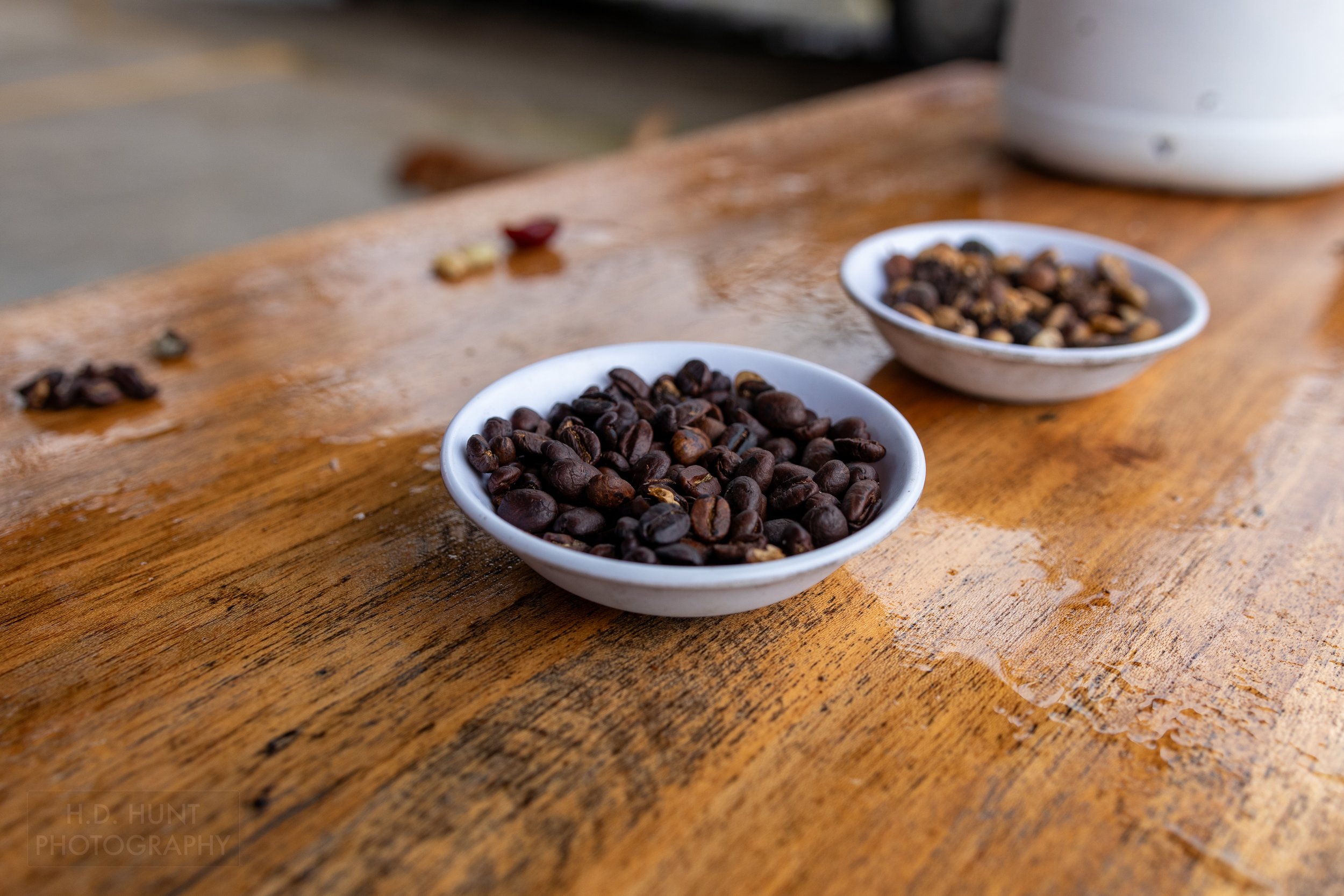 Coffee beans sit in two white dishes atop a wooden table at Mi Cafecito, Costa Rica.