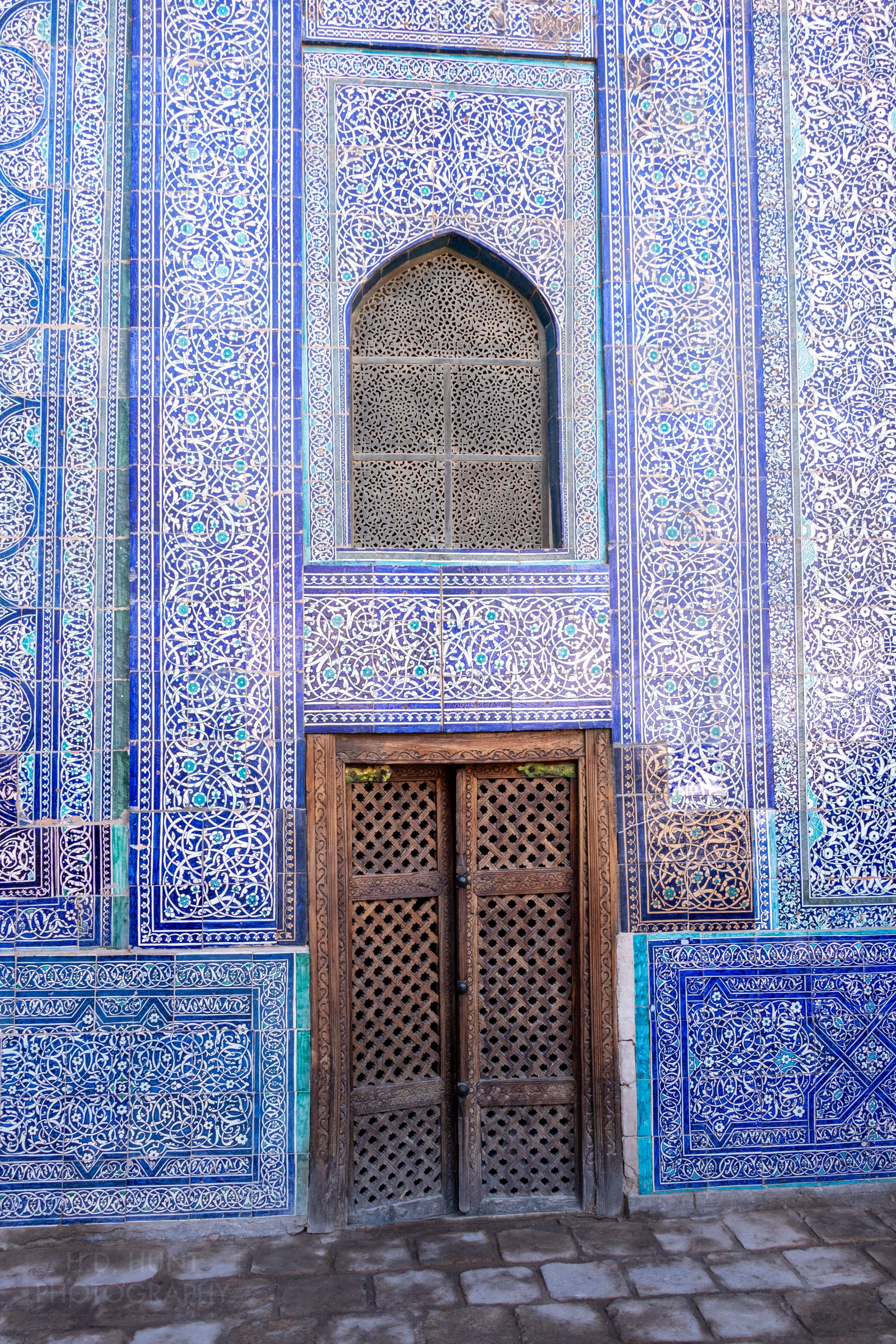 A small wooden door surrounded by blue and white tile work at Toshhovli Palace, Khiva, Uzbekistan.