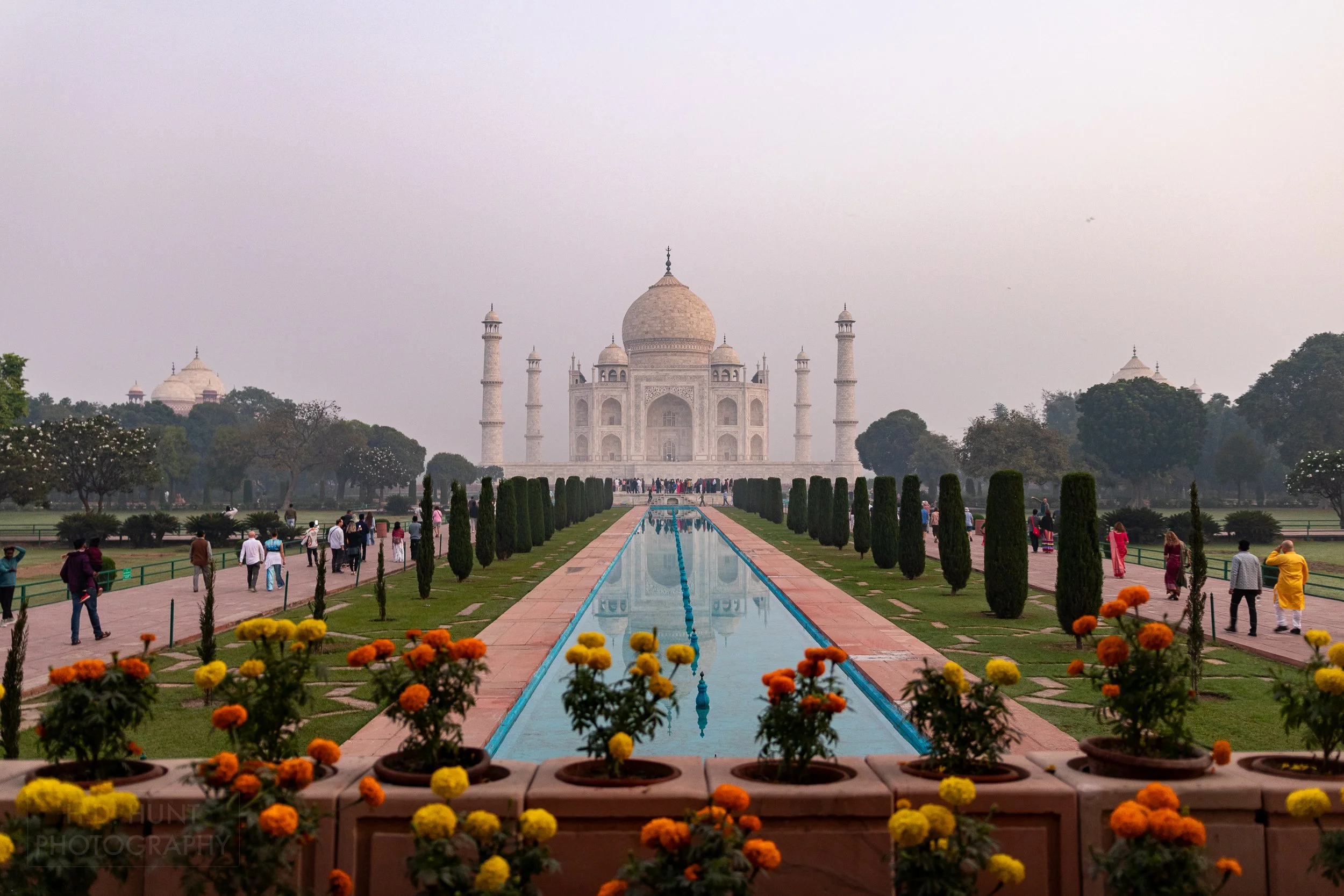 A long blue pool ringed with trees and flowers is seen in the foreground of the Taj Mahal, Agra, India.