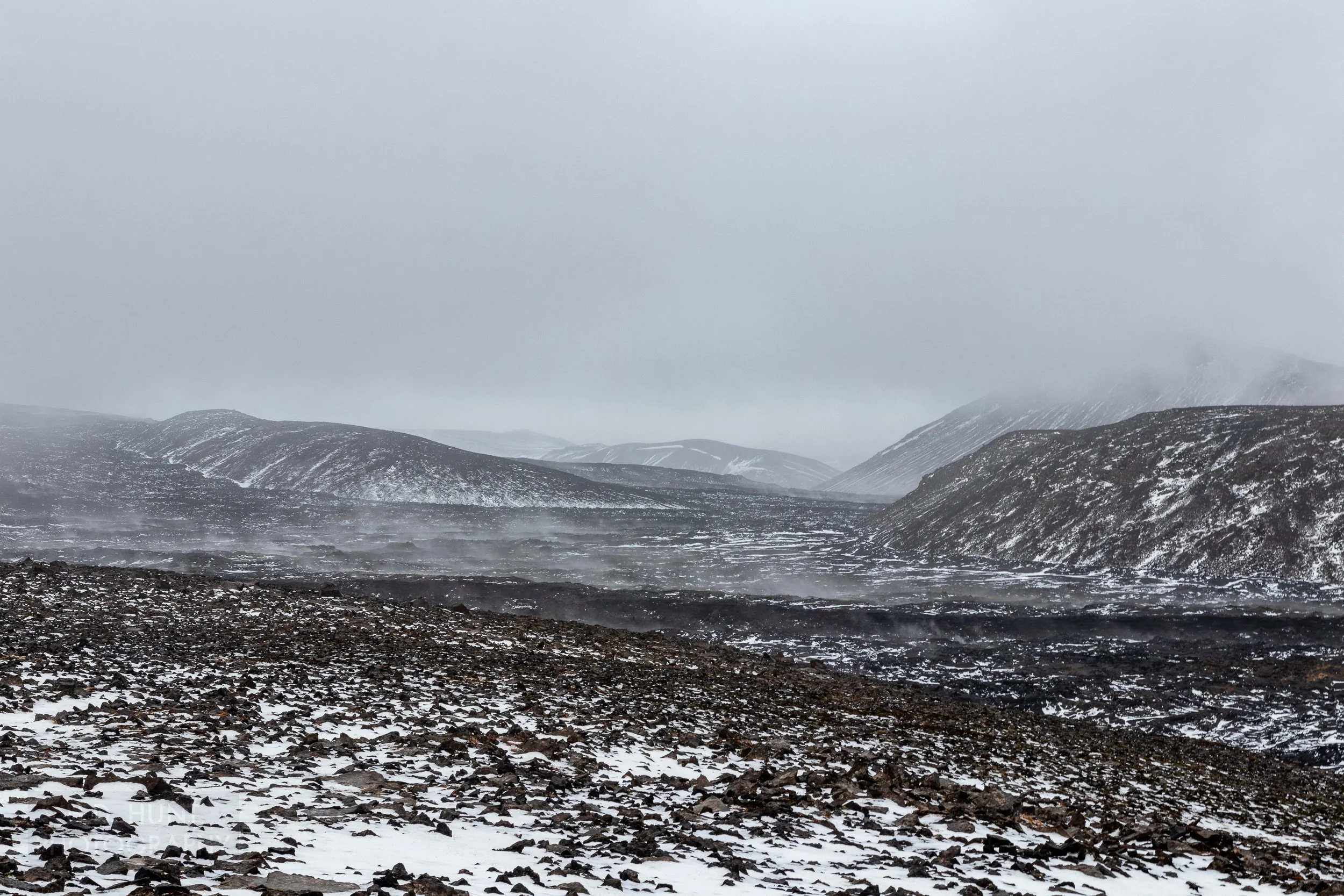 Volcano-produced steam rises from the black rock- and snow-covered earth at the Sundhnúksgígar crater chain on Reykjanes Peninsula, Iceland.