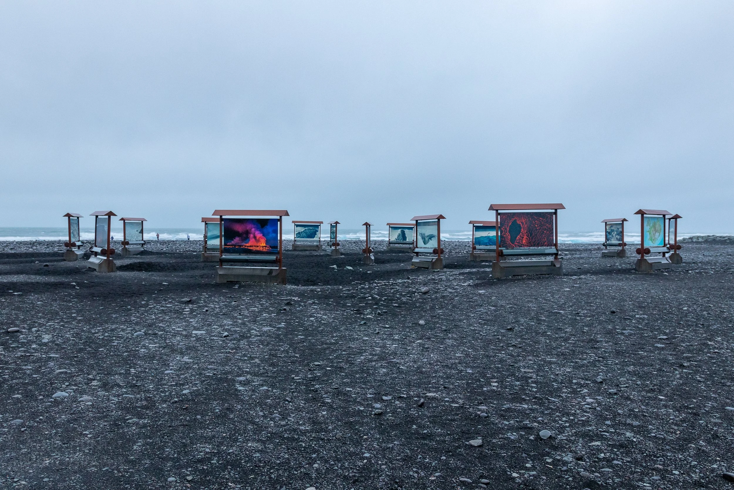 Informational signs and artwork displays sit on the black sands of Diamond Beach, Iceland.