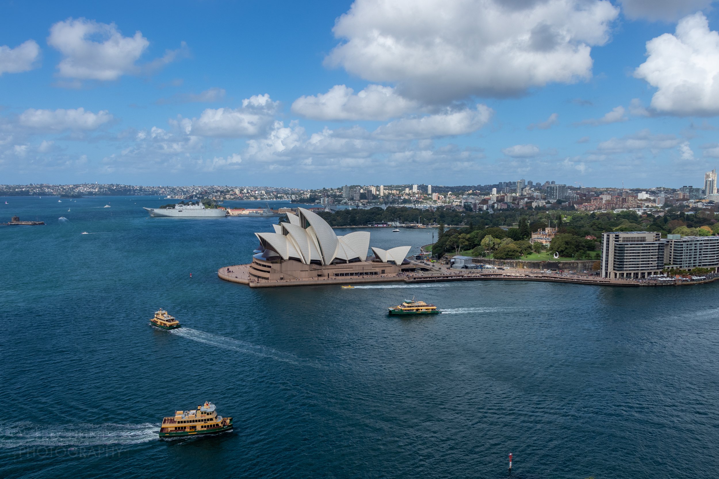 Ferry boats cross into Circular Quay in front of the Sydney Opera House beneath a cloudy sky, Sydney, Australia.