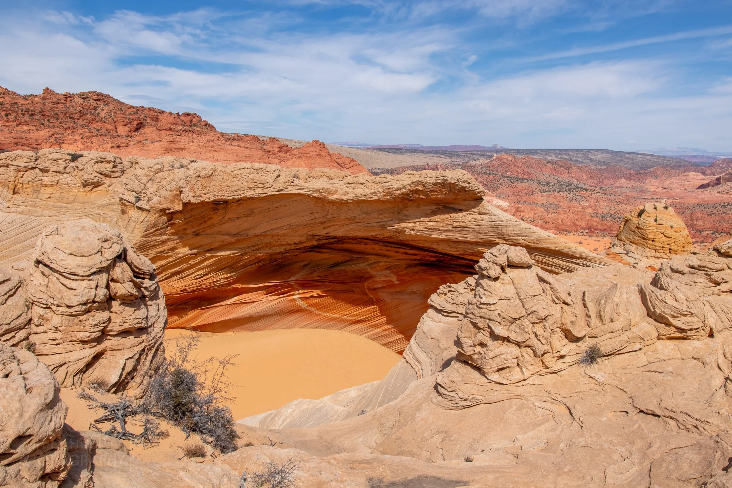A large cave-like opening is seen underneath an overhang of stripped tan sandstone within Coyote Buttes North, Paria Canyon-Vermilion Cliffs Wilderness, Arizona, United States.