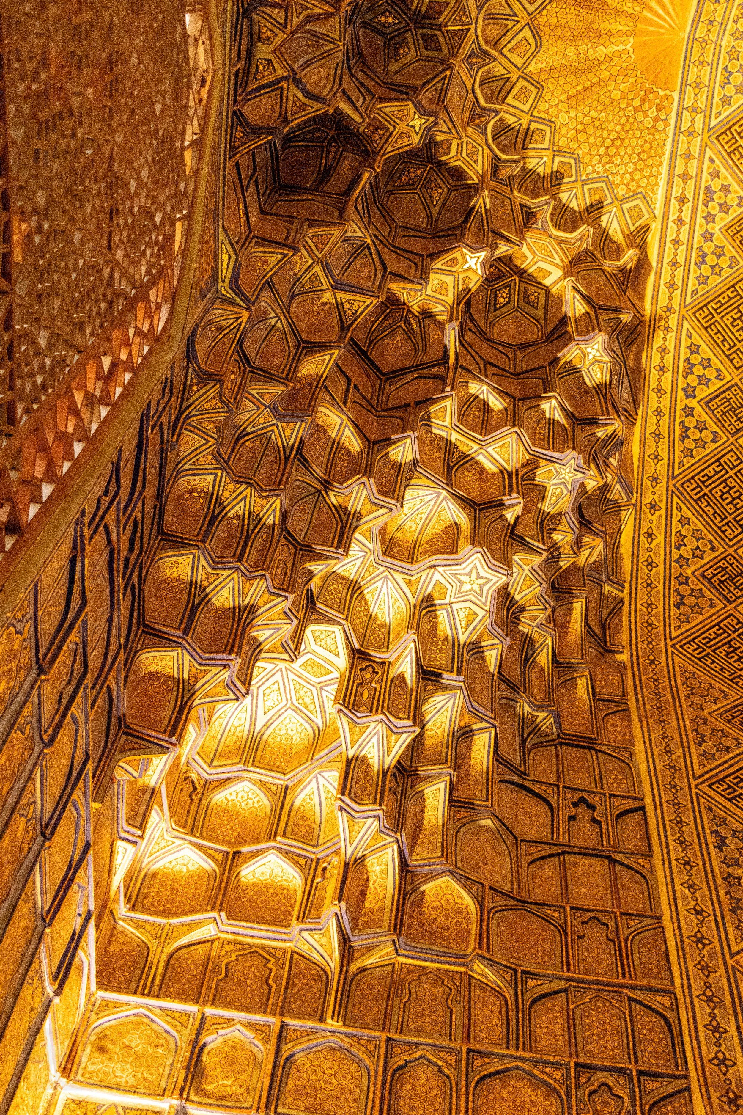 Close-up of a golden muqarnas honeycomb ceiling pattern inside Guri Amir mausoleum in Samarkand, Uzbekistan.