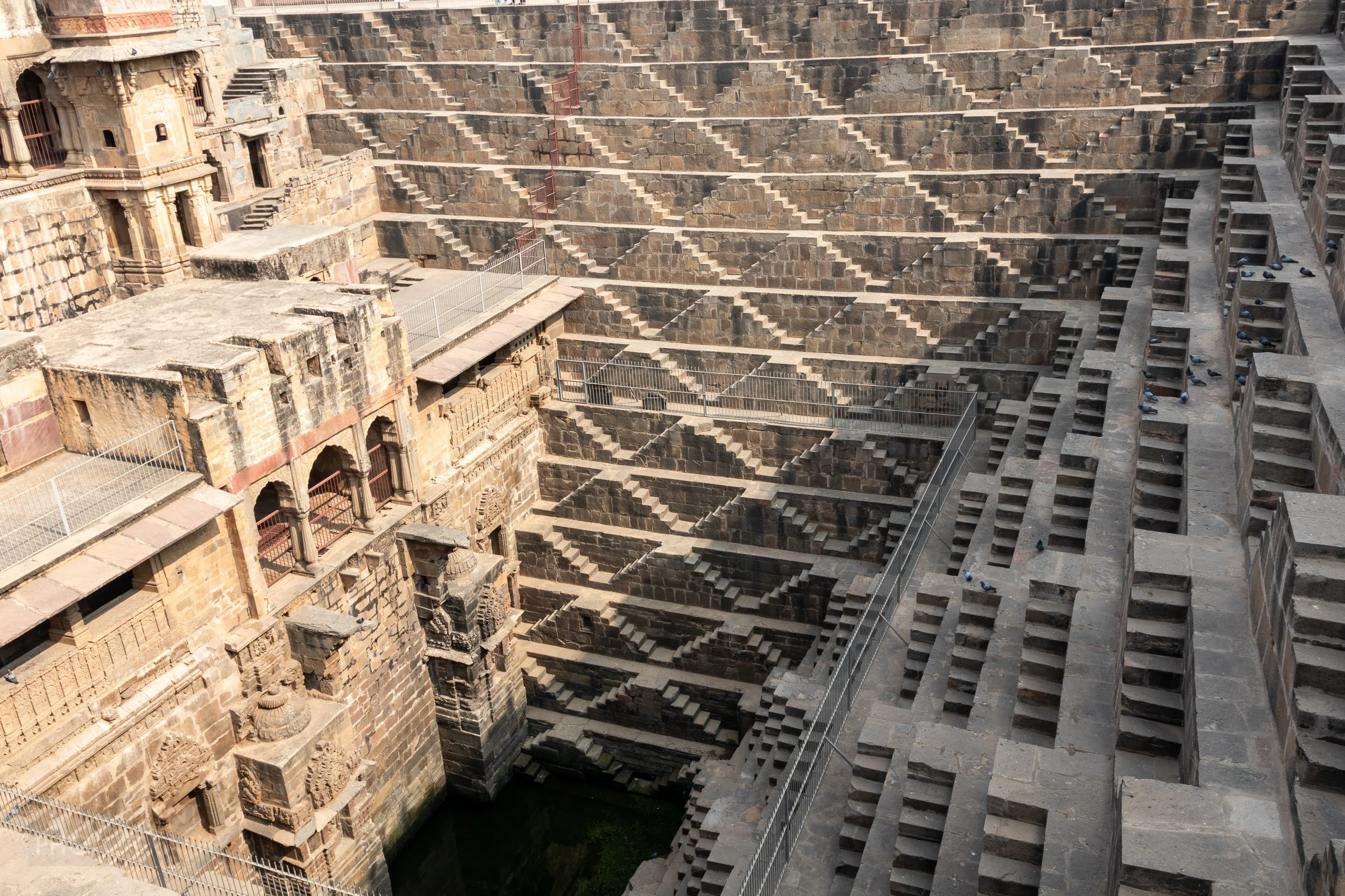 The zig-zag tan stone steps of Chand Baori rise from a small water well in the ground, Abhaneri, India.
