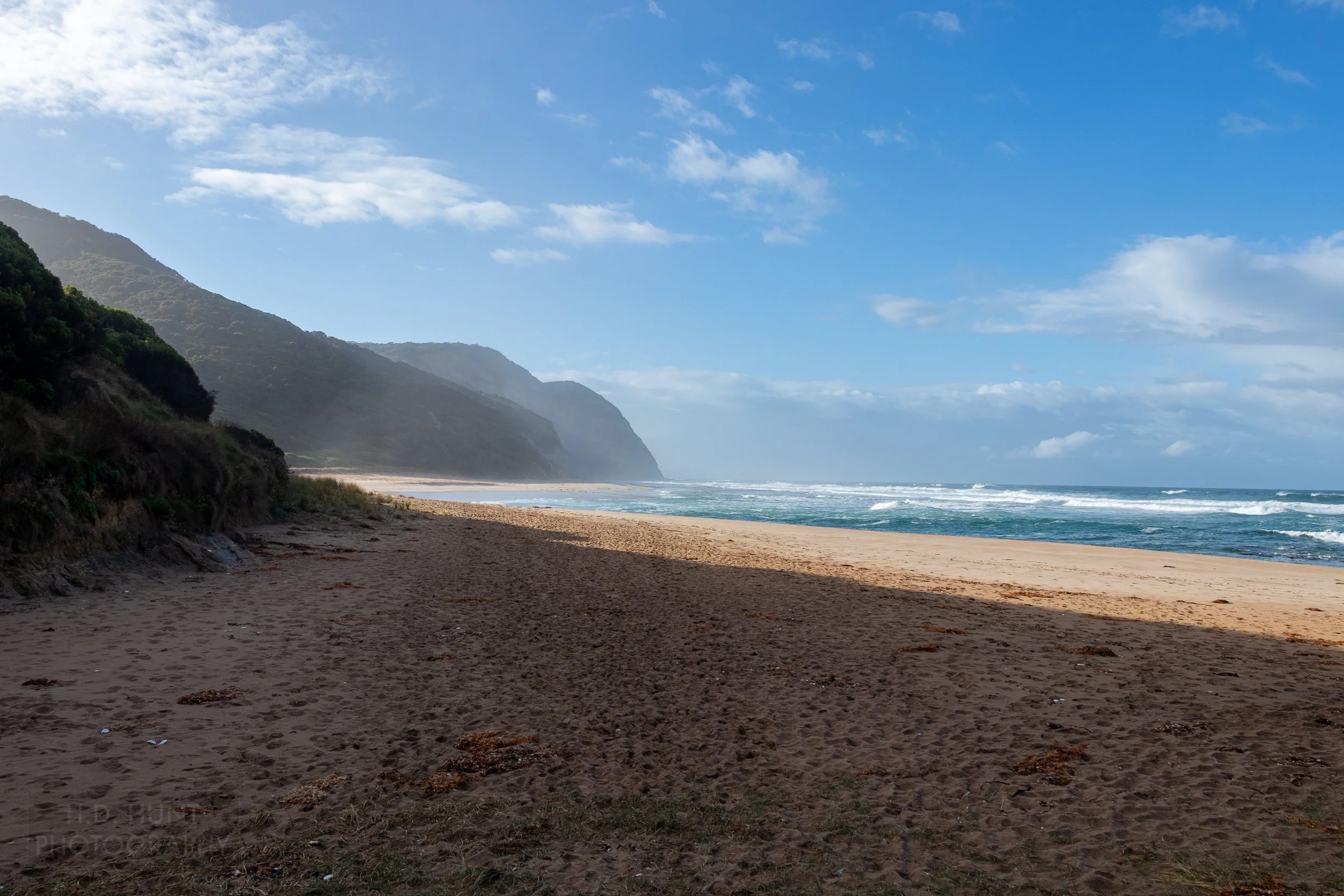 Spray from the Southern Ocean flies over a wide beach along The Great Ocean Walk, Victoria, Australia.
