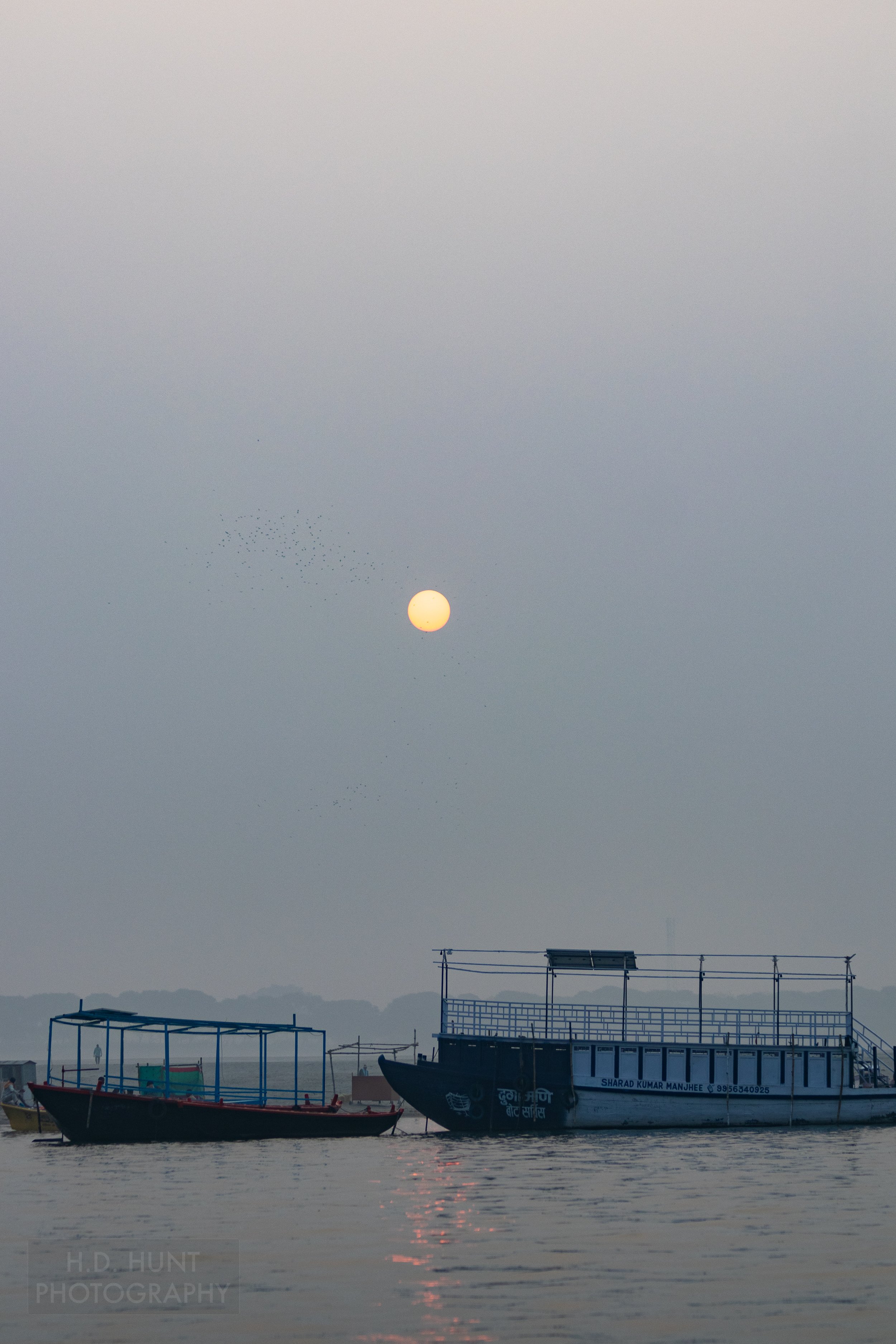 The sun rises over two boats in the Ganges River, Varanasi, India.
