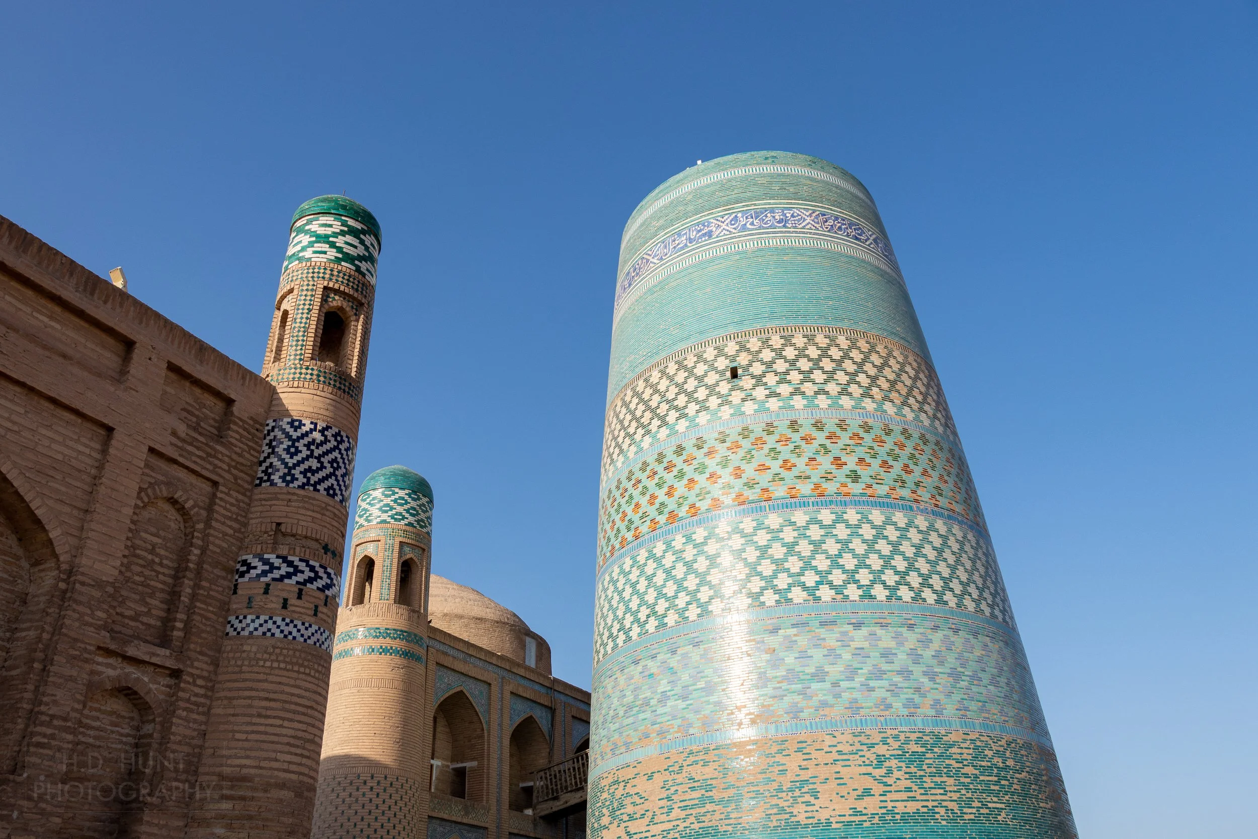 The blue, green, and tan tiles of Kalta Minor can be seen as it rises above Khiva, Uzbekistan.