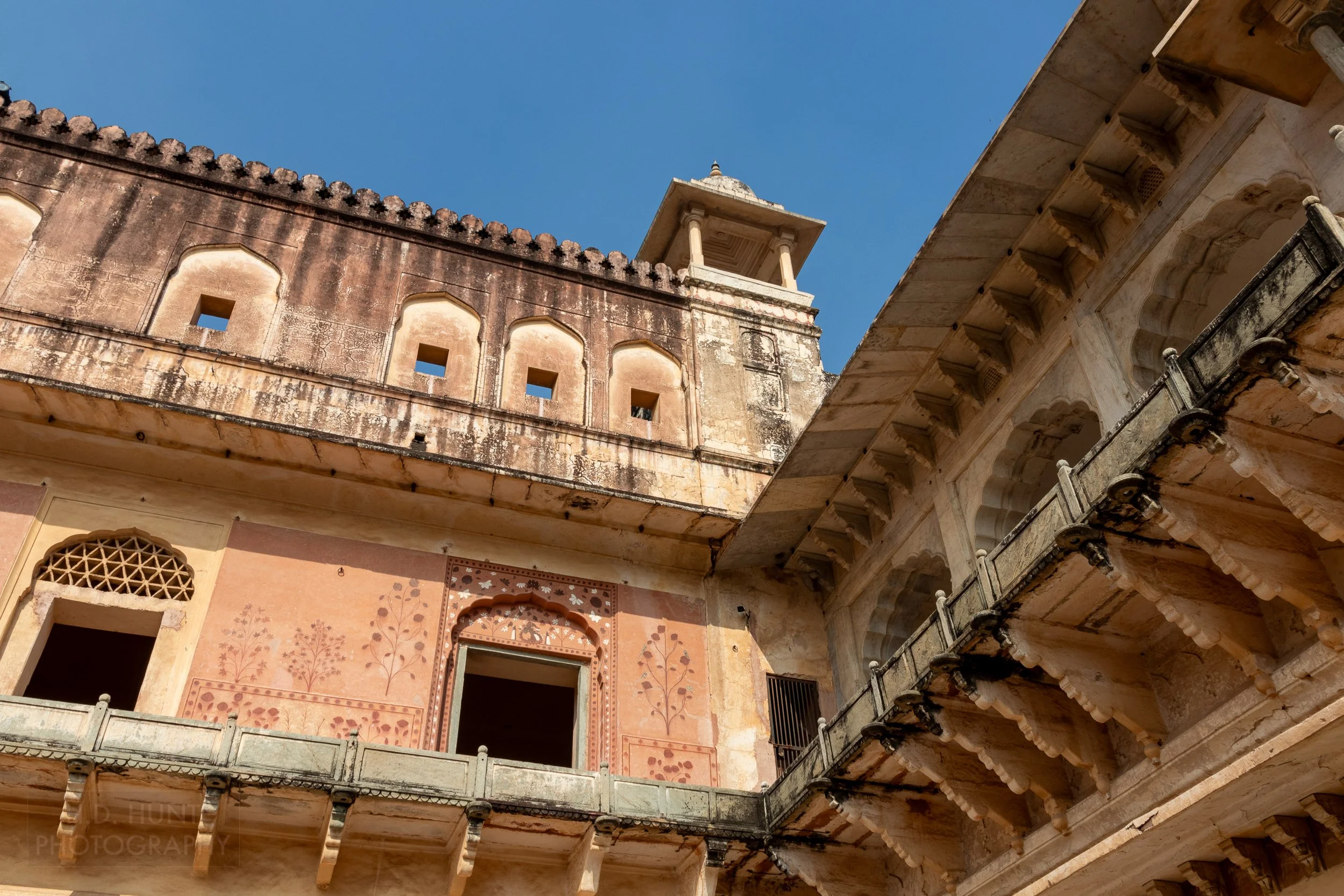 A pink and yellow wall and balcony rise above a courtyard, Amber Fort, Amer, India.
