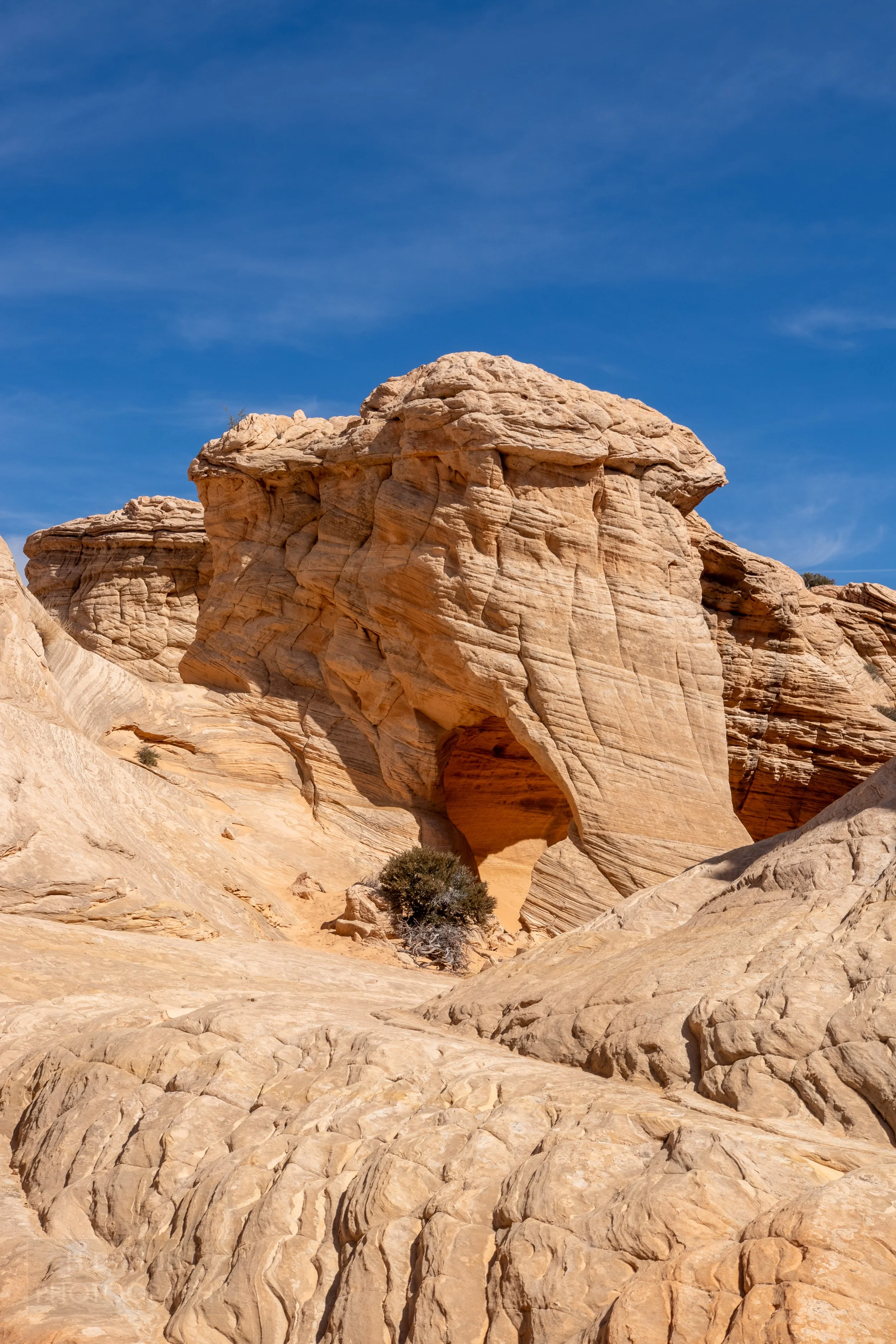 A large white sandstone rock cliff features an opening at its bottom with heavily eroded walls in Coyote Buttes North, Paria Canyon-Vermilion Cliffs Wilderness, Arizona, United States.