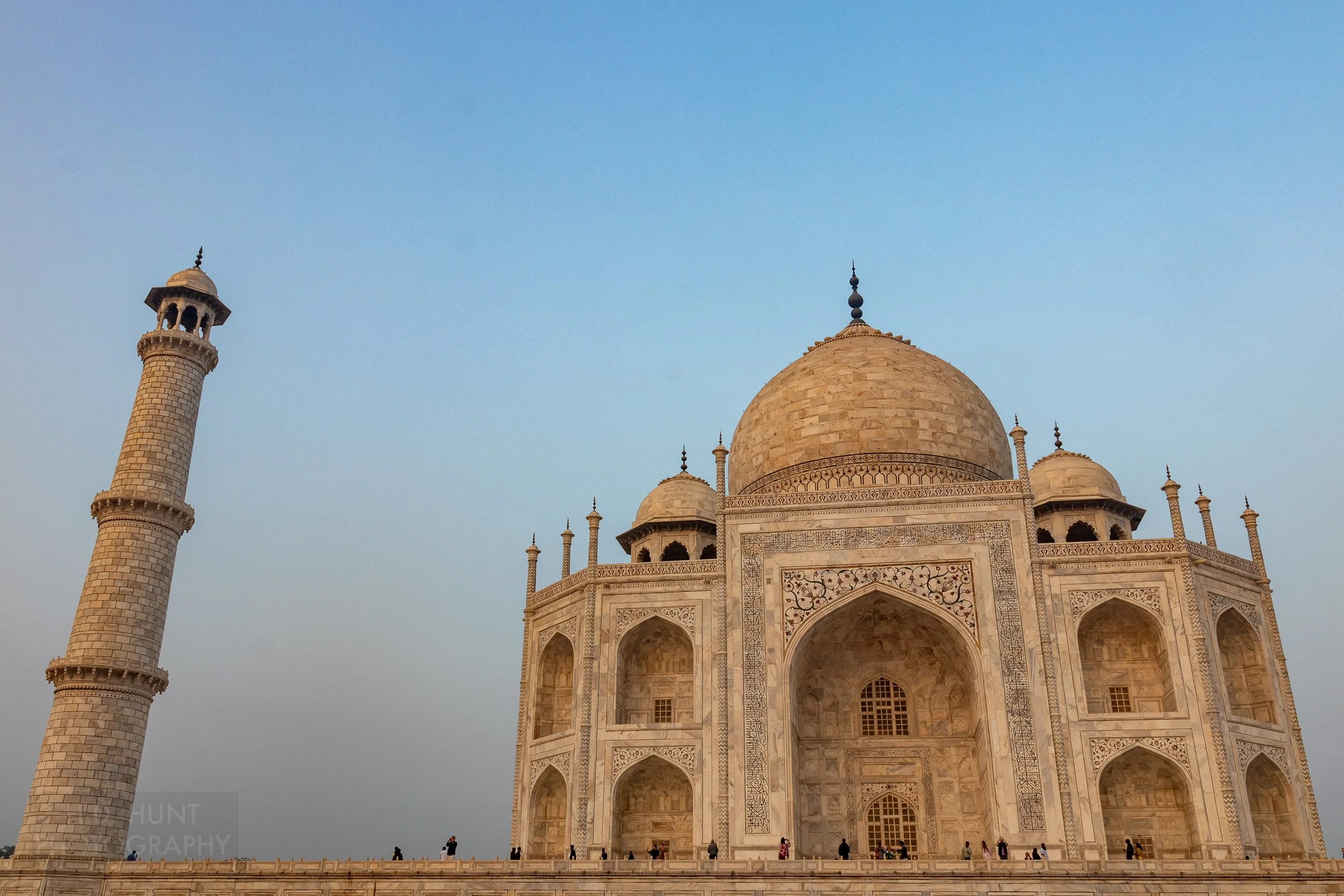 The main white marble mausoleum building of Taj Mahal and a minaret are set against a light blue sky, Agra, India.