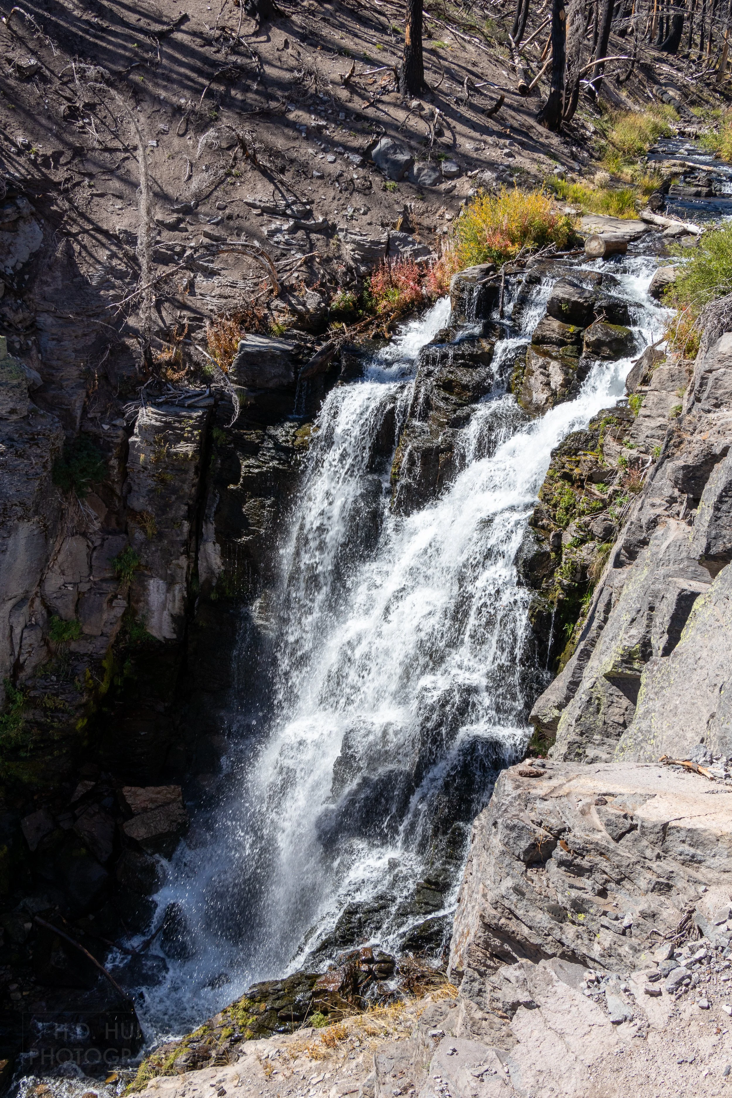 Water cascades over a waterfall between dark-colored rock edges, Lassen Volcanic National Park, California, United States.