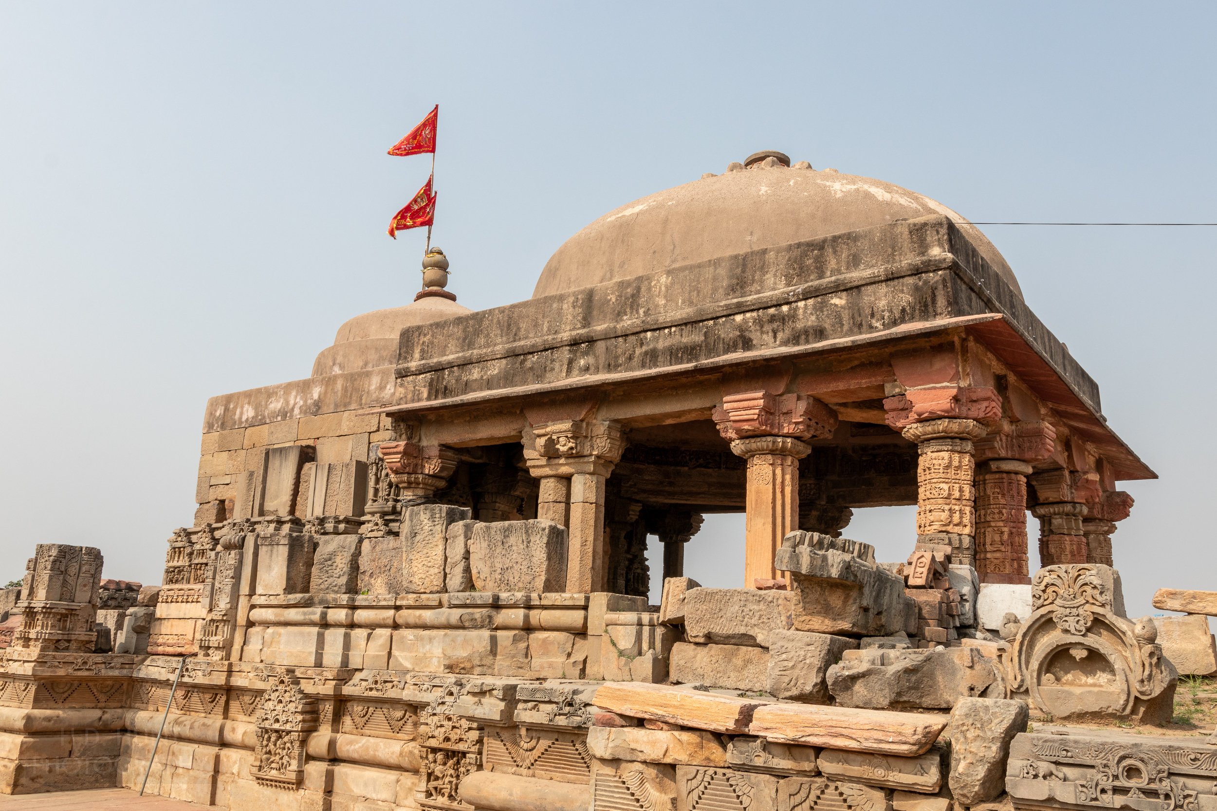A tan stone temple with a round dome roof and two red flags, Abhaneri, India.