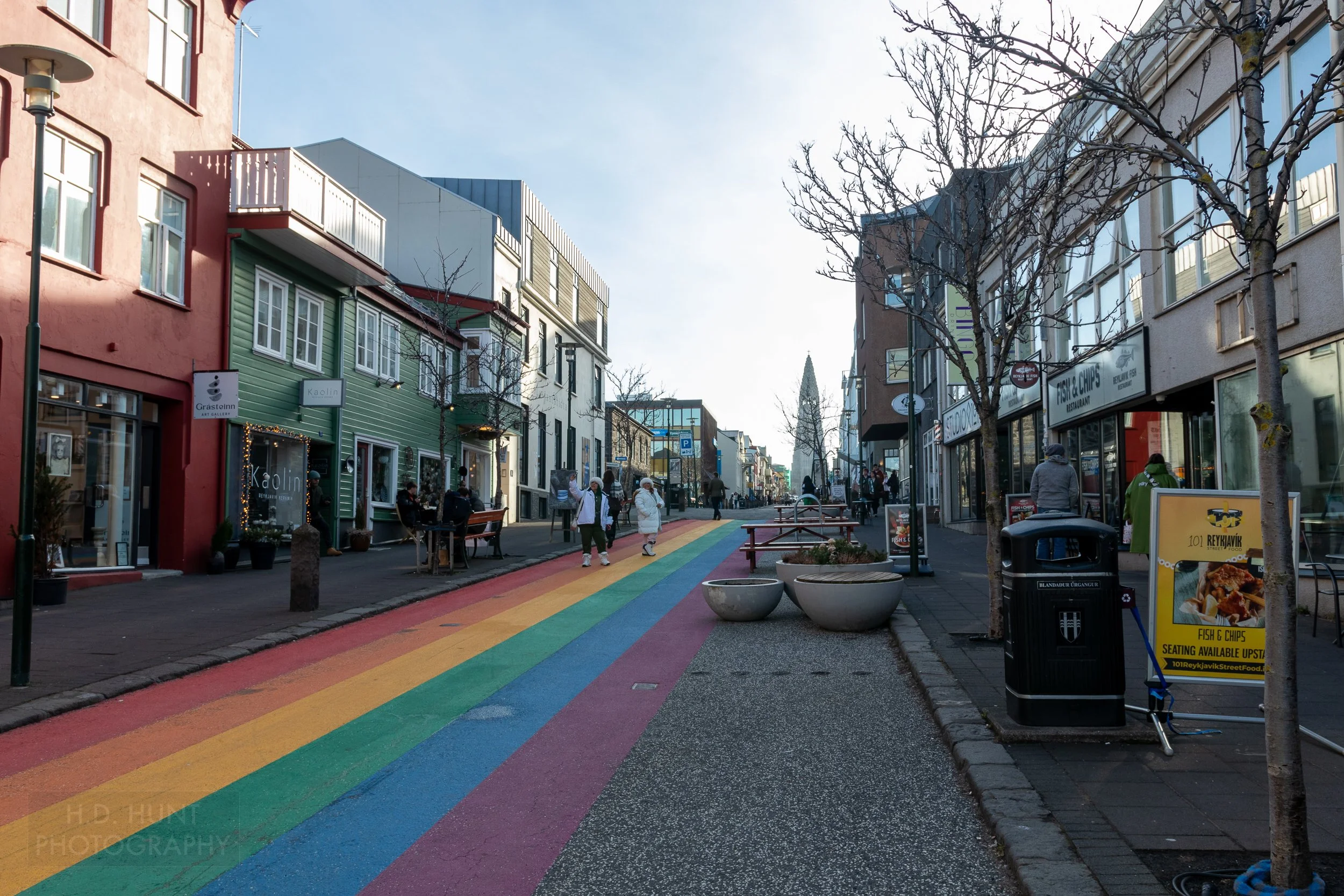 A photograph of a road with a rainbow painted on the roadbed, called Skólavörðustígur, Reykjavík, Iceland.