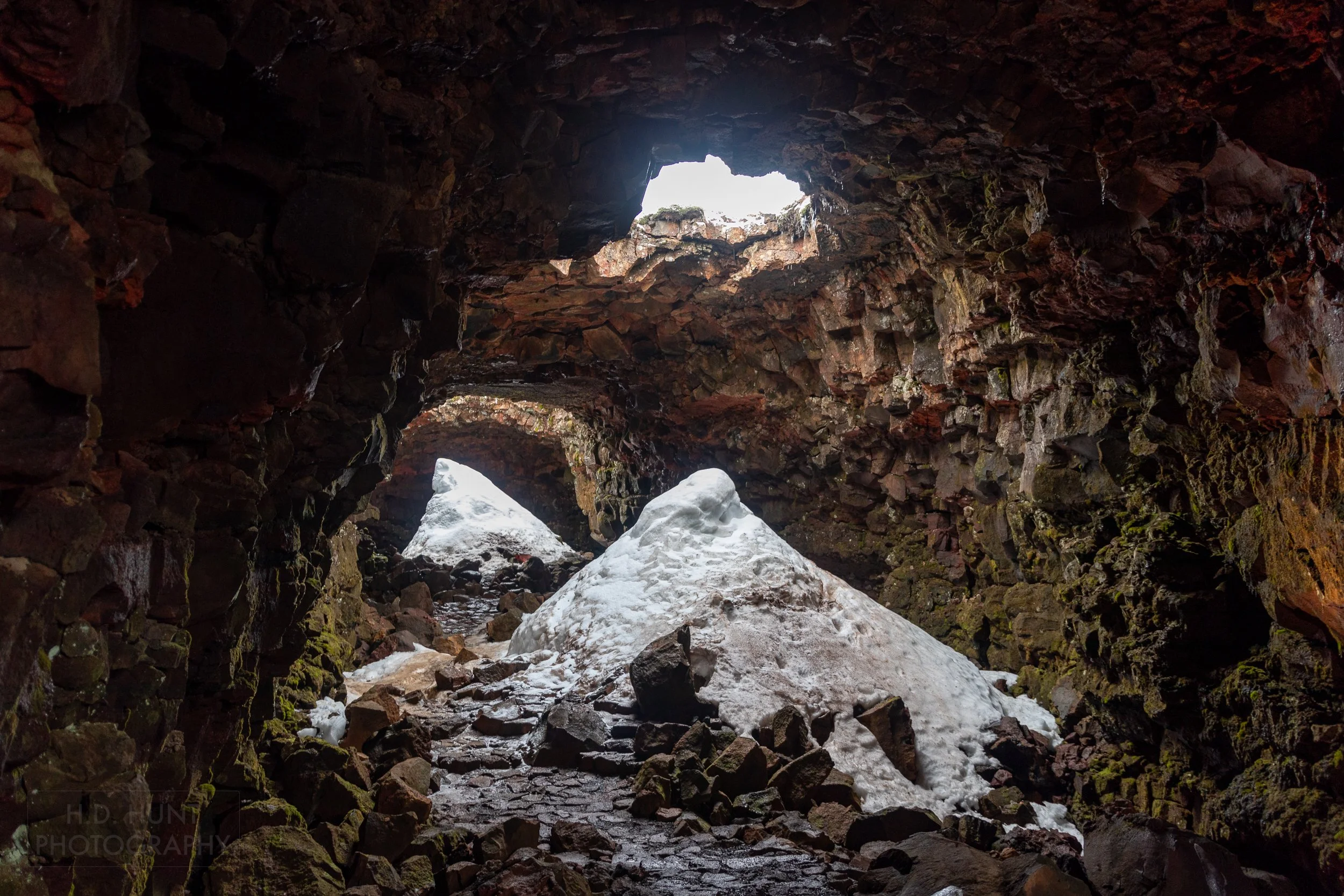 The interior of the Raufarhólshellir lava tube, featuring large piles of snow from precipitation which fell through holes in the ceiling of the lava tube, Iceland.
