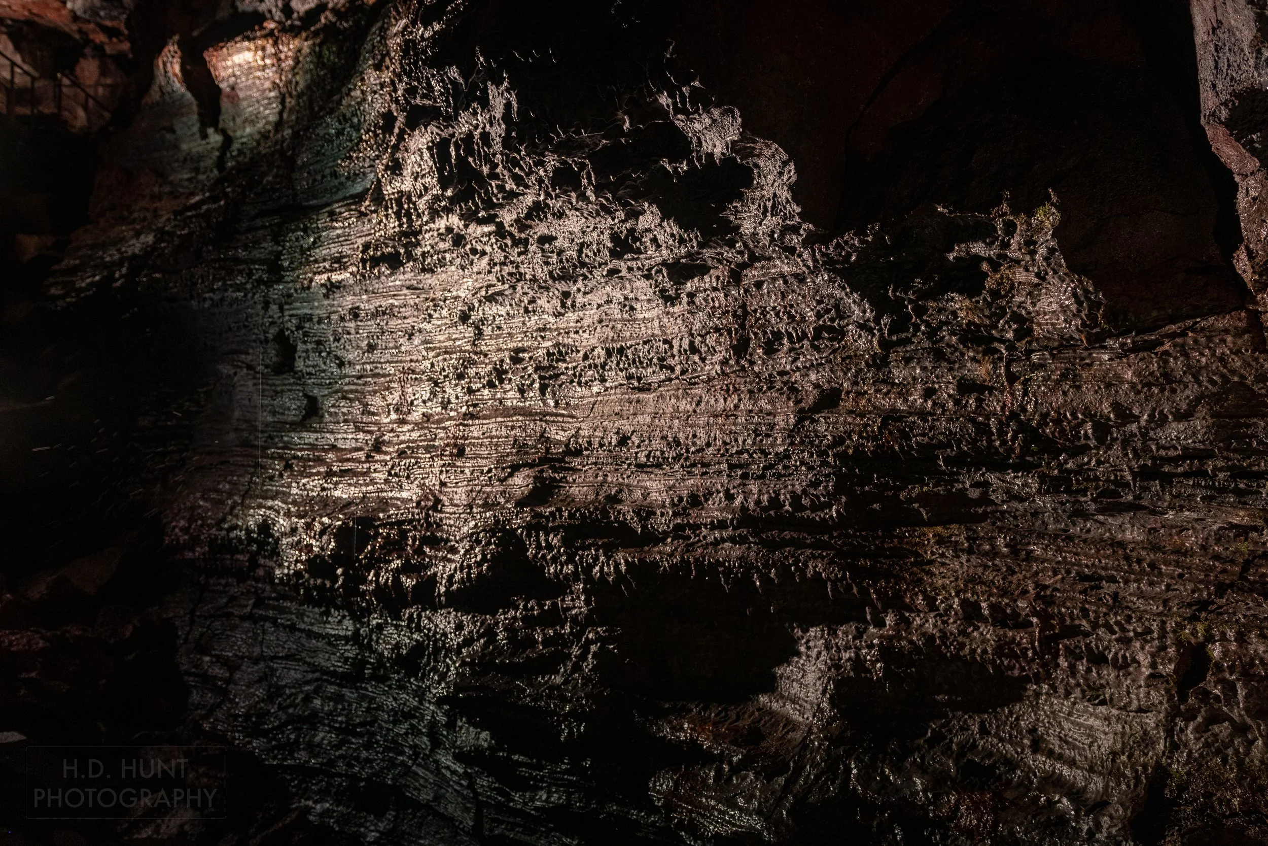 A highly-textured dark colored wall is seen within the lava tube Raufarhólshellir, Iceland.