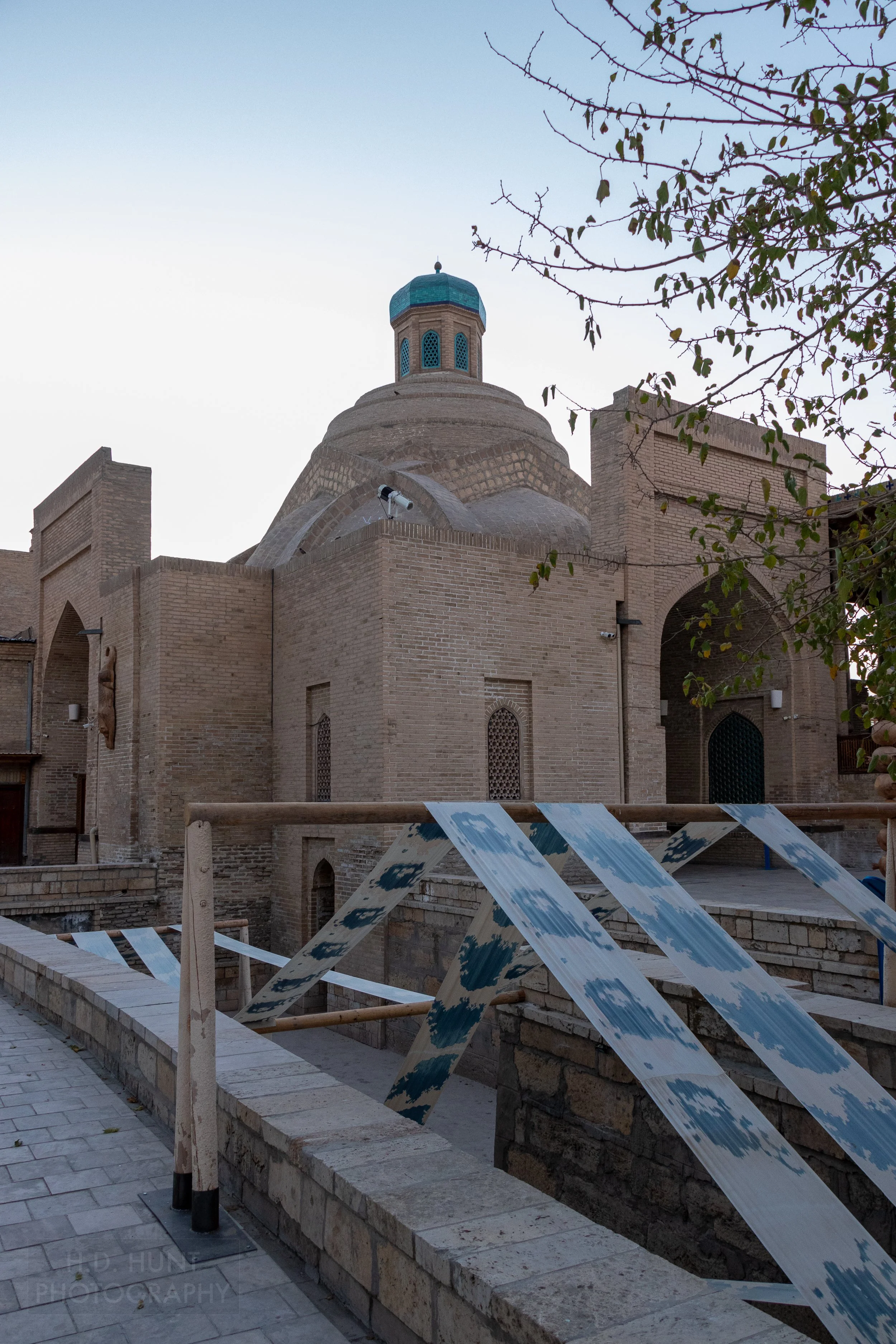 A blue and white textile art display hangs over wood beams in a square in Bukhara, Uzbekistan.