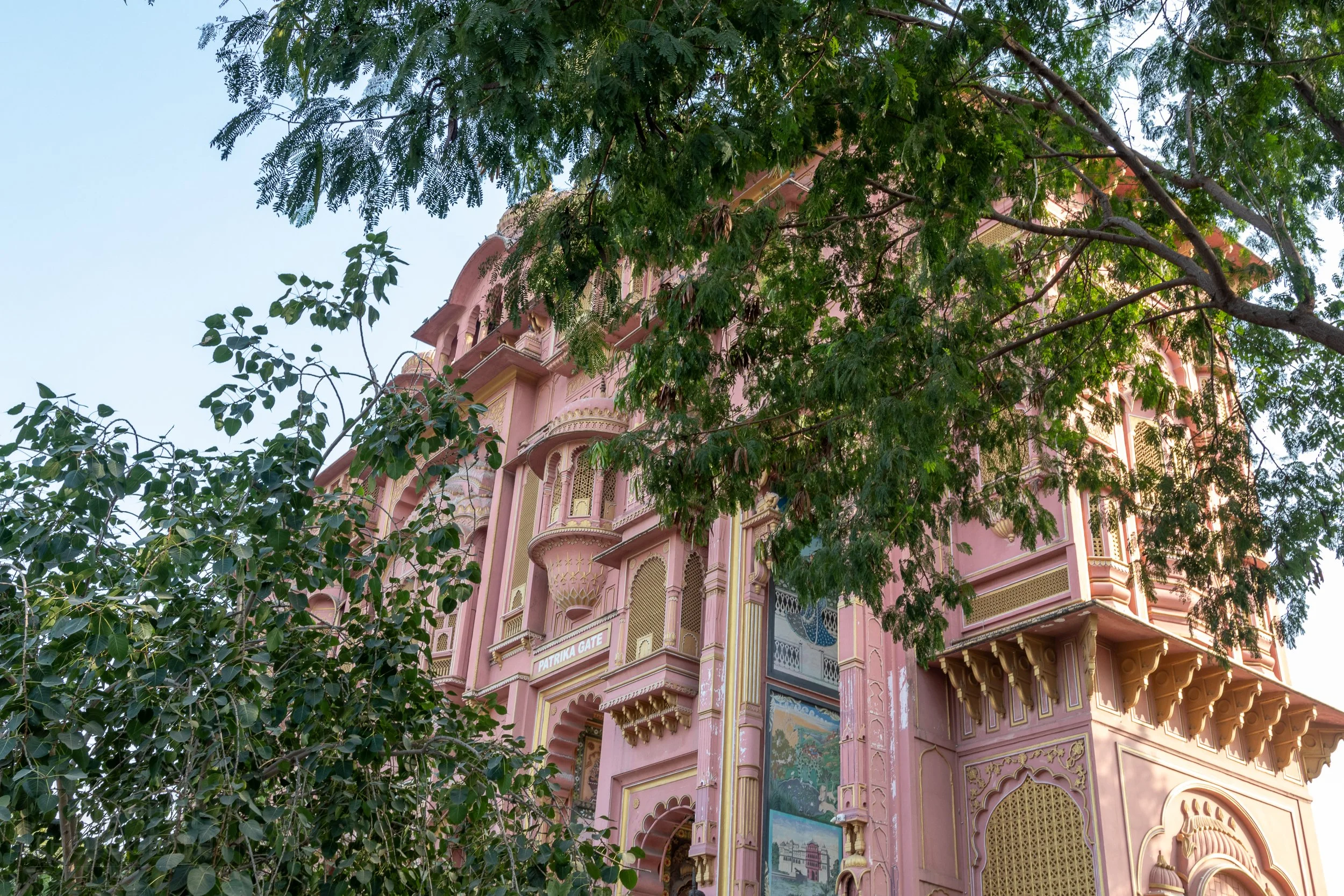 The pink facade of the Patrika Gate is seen behind trees in Jaipur, India.