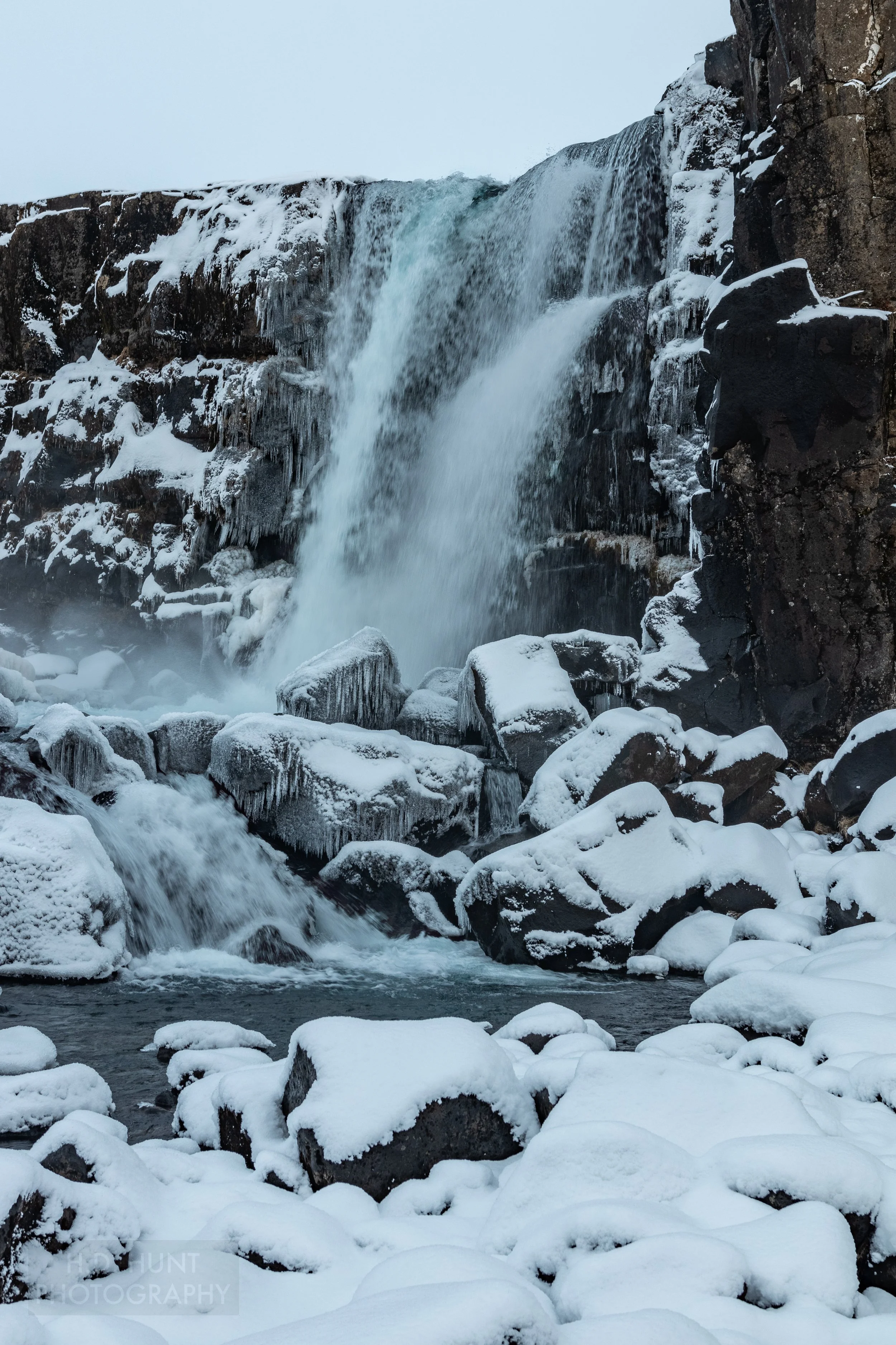A waterfall cascades over snow- and ice-covered black rock at Þingvellir, Iceland.