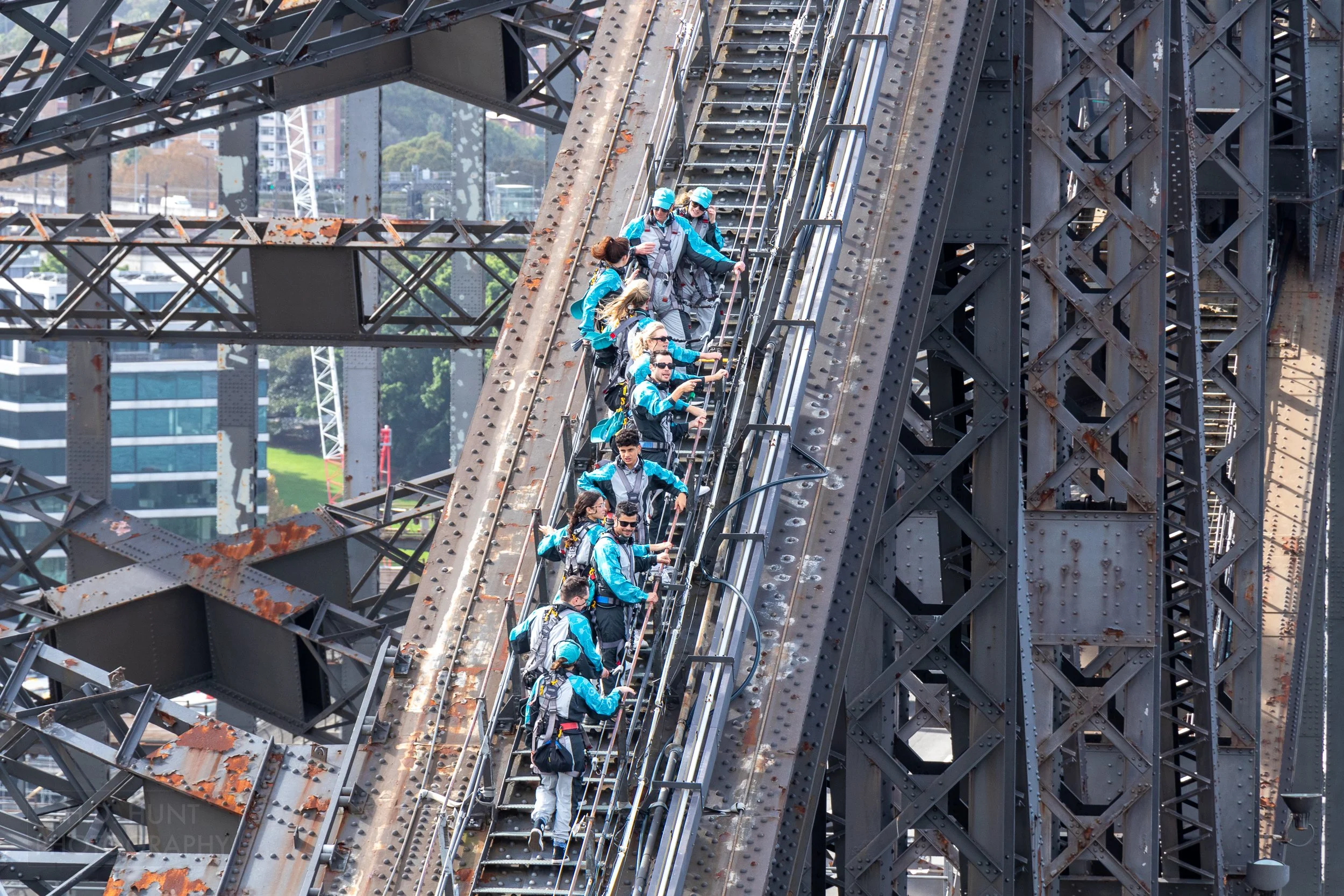 Several visitors clad in light blue jumpsuits climb the outer steel support of the Sydney Harbour Bridge, Sydney, Australia.