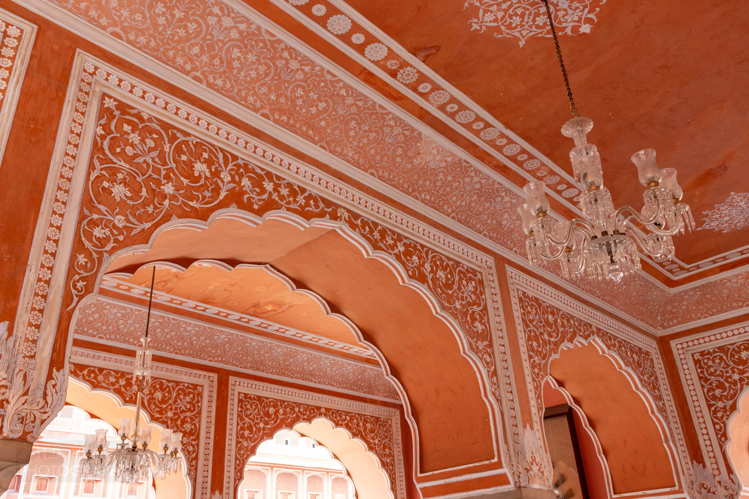 A bright orange-red and white wall with several arches, City Palace, Jaipur, India.