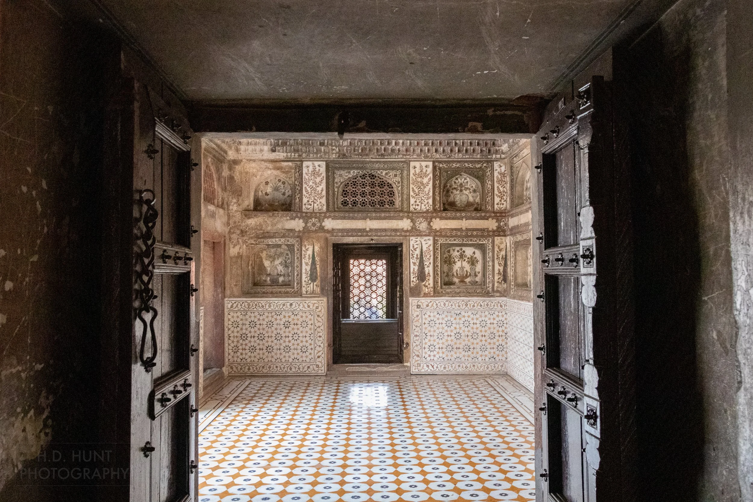 A bright colored room featuring white, black, and yellow floor tiles is seen through a wooden door archway at the Tomb of I’timad-ud-Daulah, Agra, India.