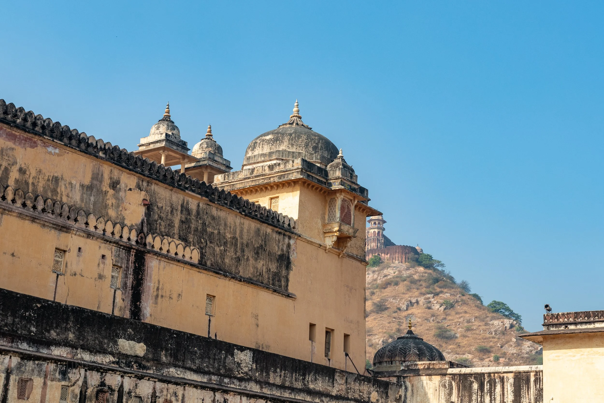 A yellow and black wall topped with multiple cupolas is seen in Amber Fort, Amer, India.