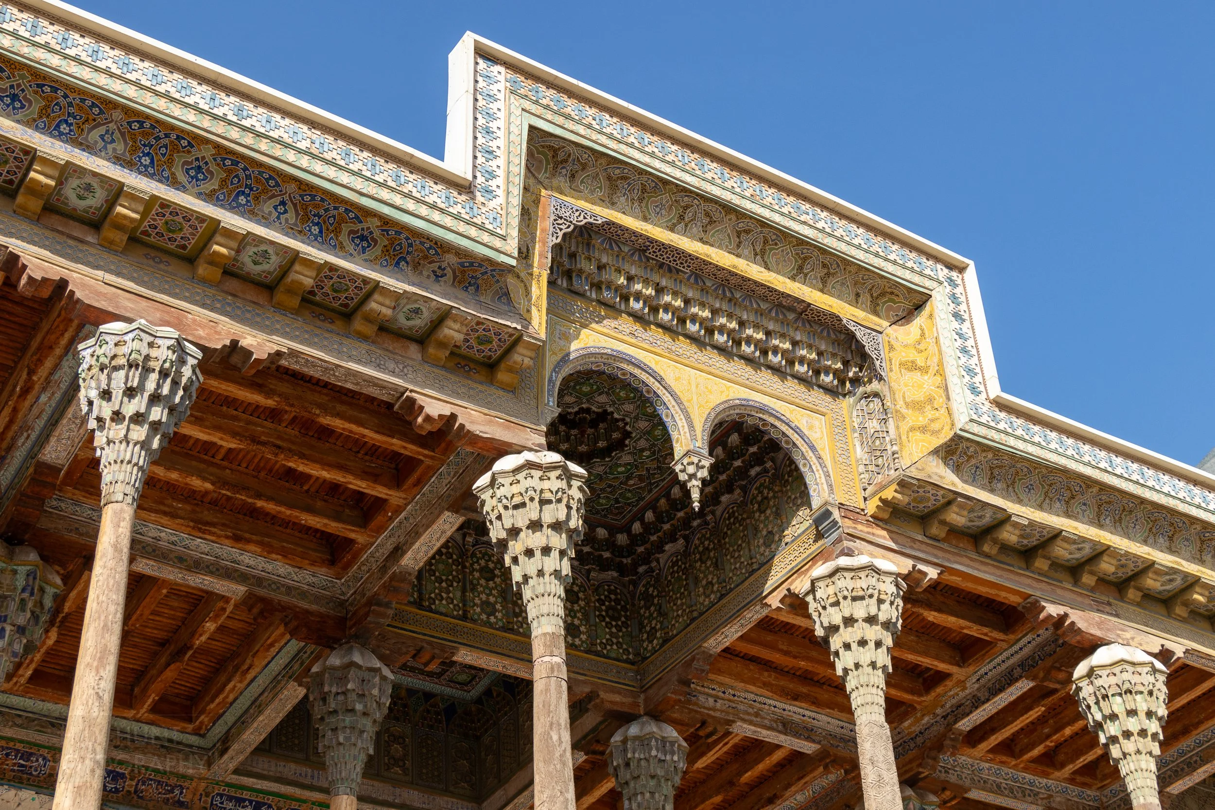Several ornate columns support the brightly-colored covered entrance of the Bolo Hauz Mosque, Bukhara, Uzbekistan.