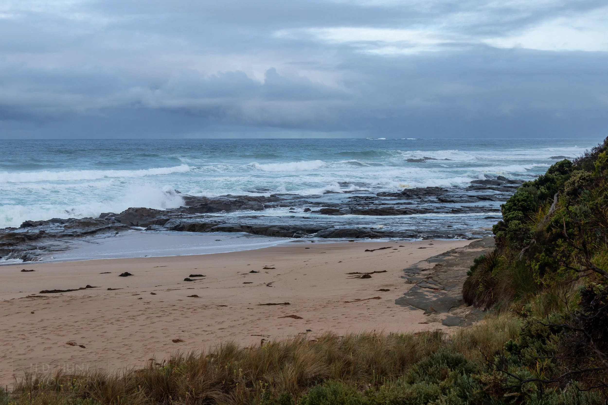 A wide sand beach underneath cliffs gives way to rocks and surf along The Great Ocean Walk, Victoria, Australia.