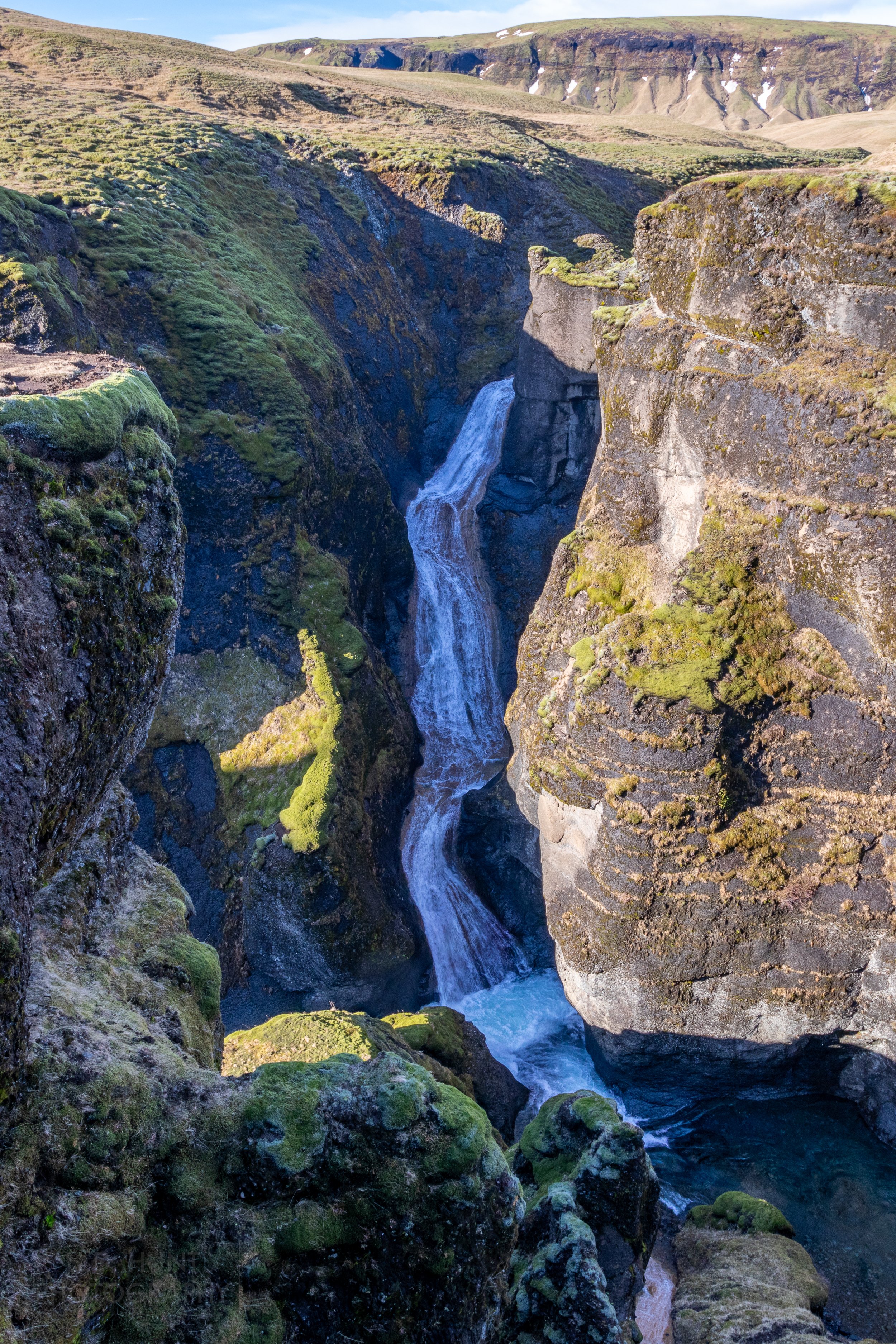 A waterfall is seen tumbling into a steep rock canyon, Fjaðrárgljúfur, Iceland.