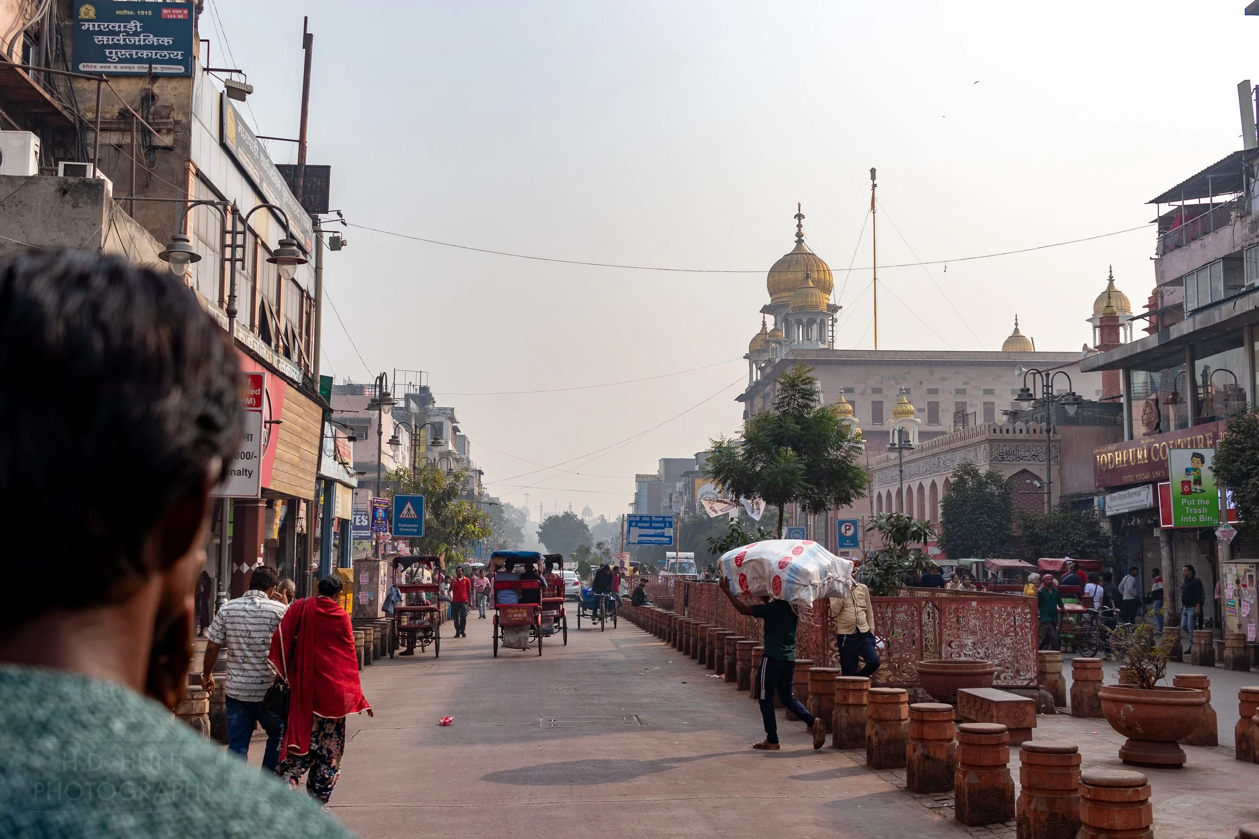 A man carries a large bag across a street, Chandni Chowk, Delhi, India.