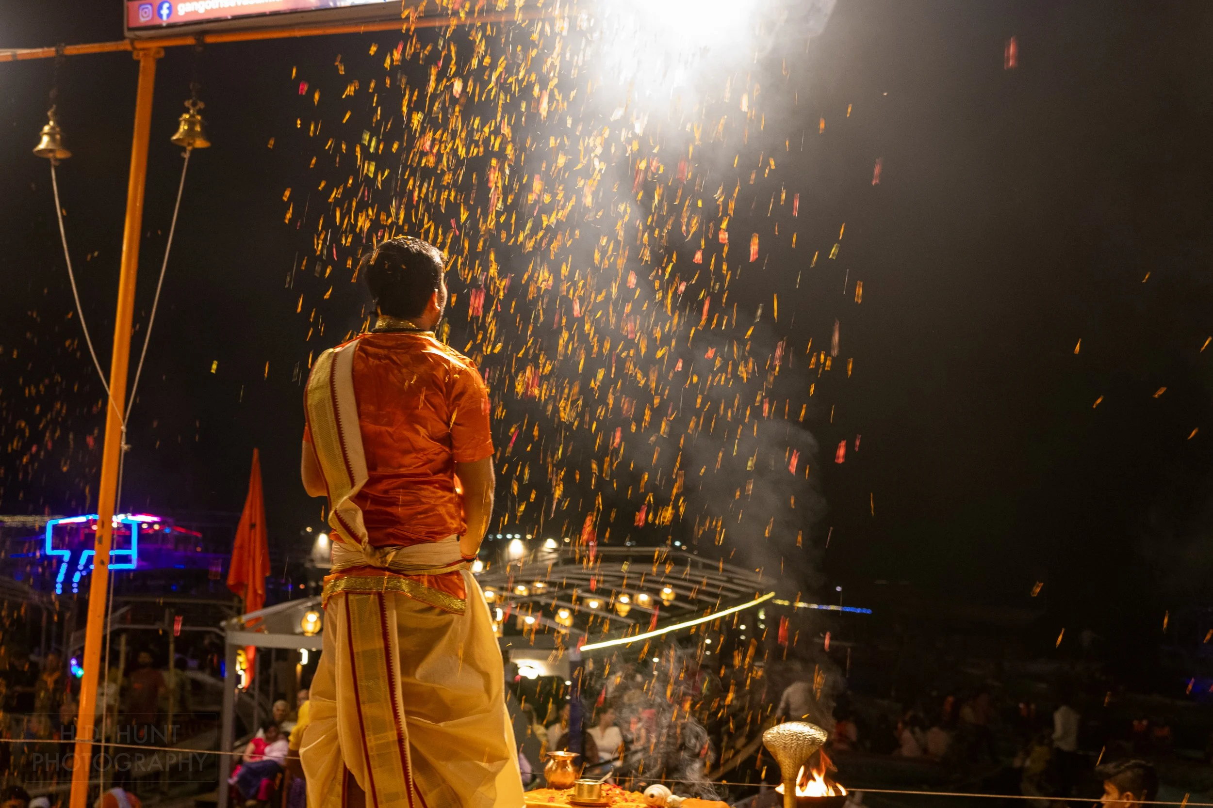 A man wearing an orange religious outfit throws flowers during a Hindu religious ceremony called arti, Varanasi, India.