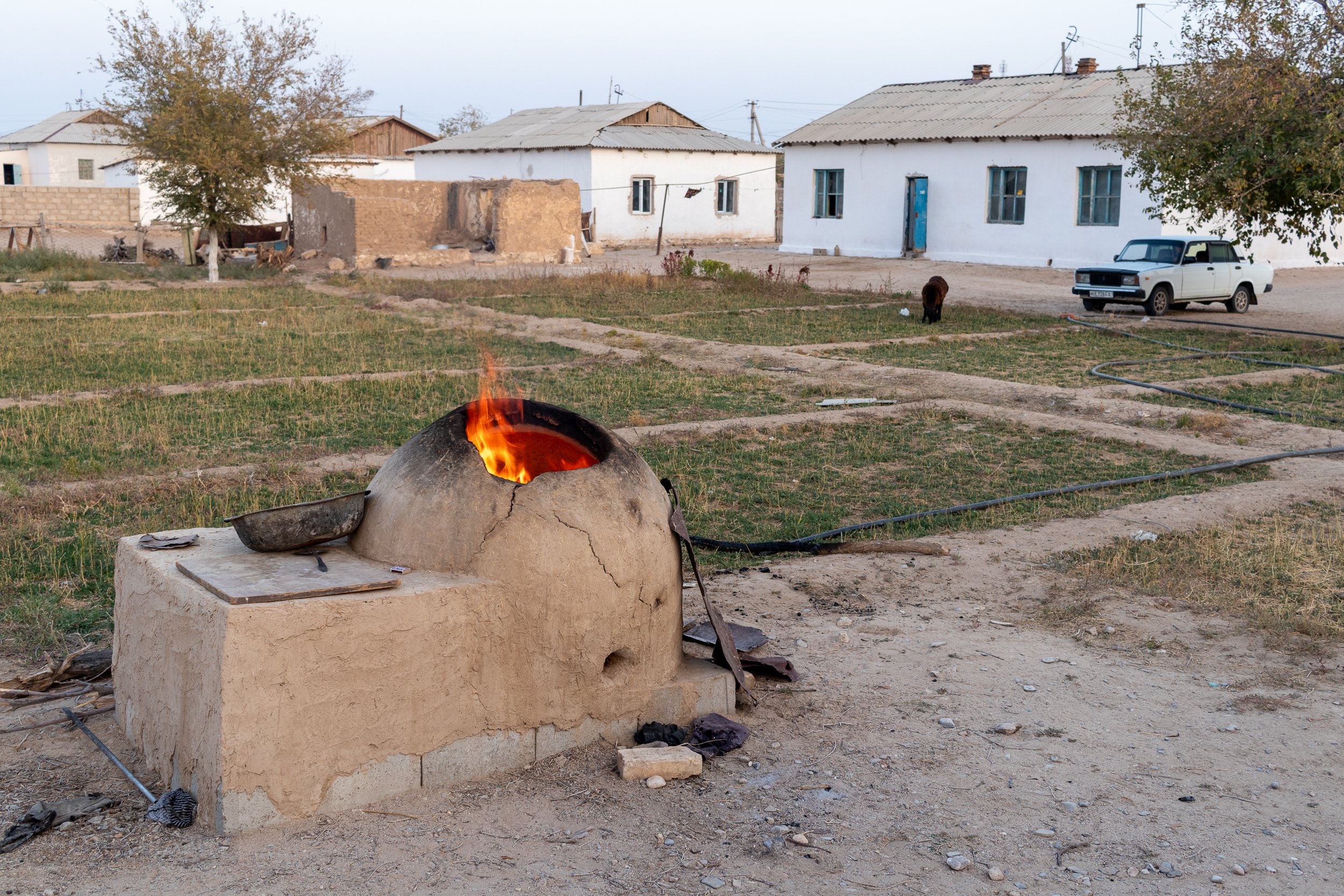 A lit clay tandoor oven sits in an outdoor courtyard in Yangikazgan, Uzbekistan.