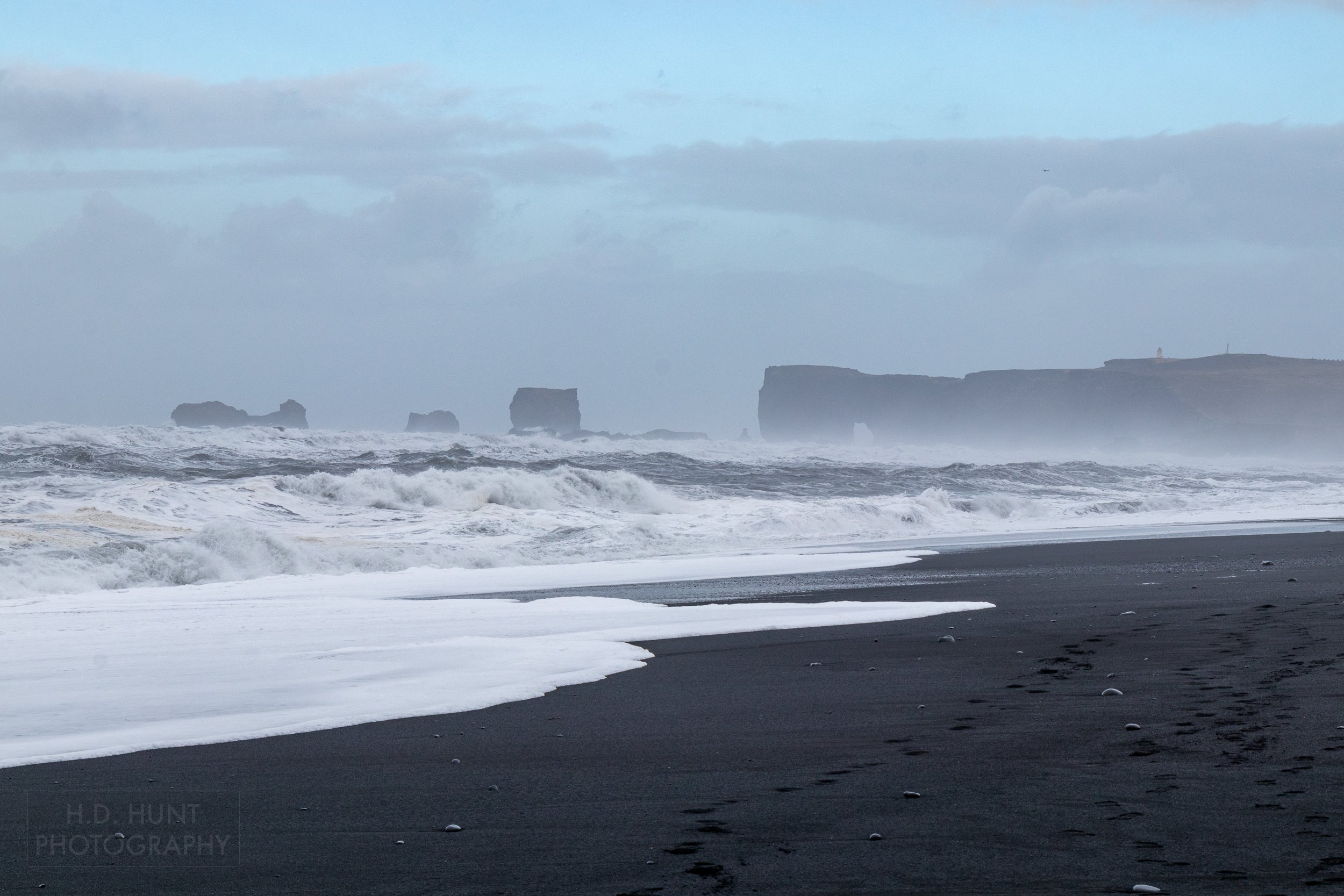 Large whitecap waves crash against a dark sand beach at Reynisfjara, Iceland