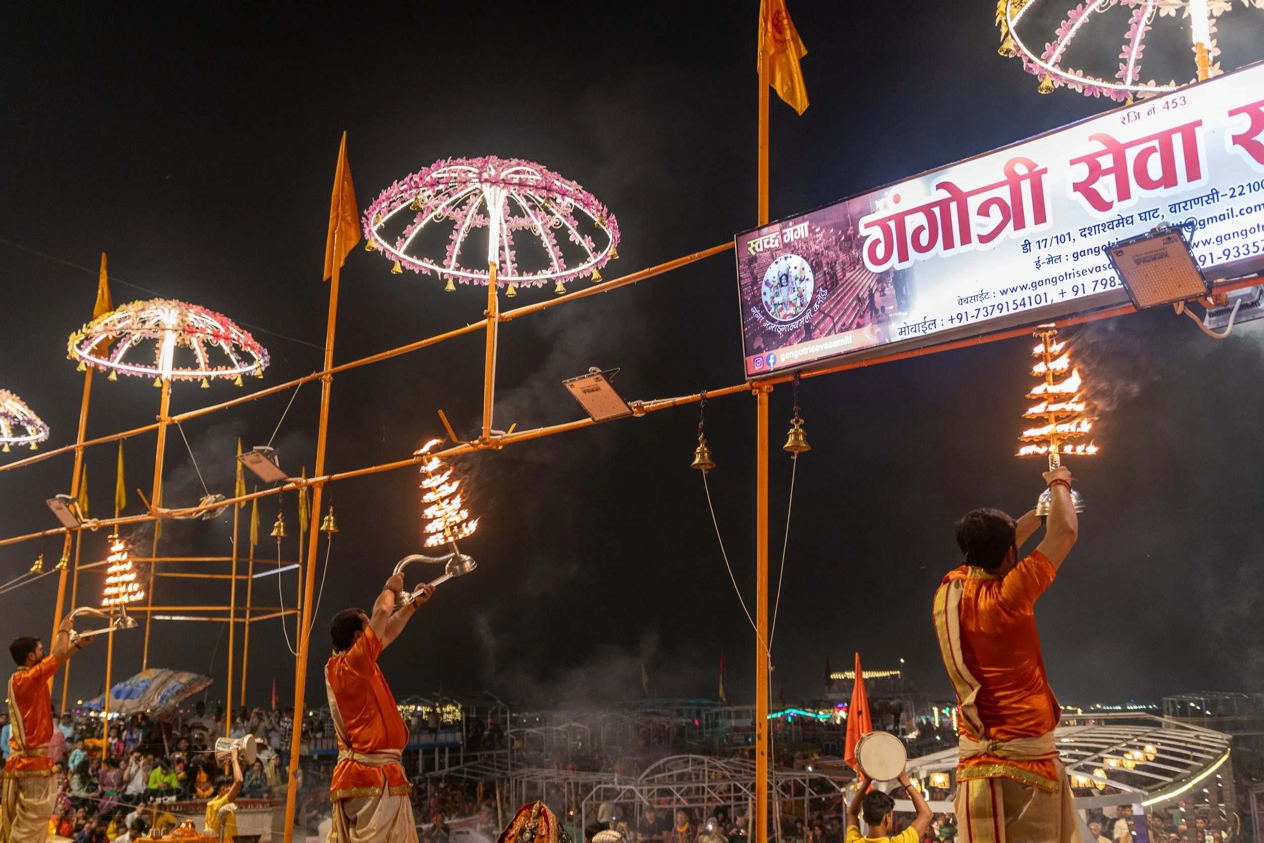 Three men hold large metal candle holders above their heads during a Hindu religious ceremony called arti, Varanasi, India.