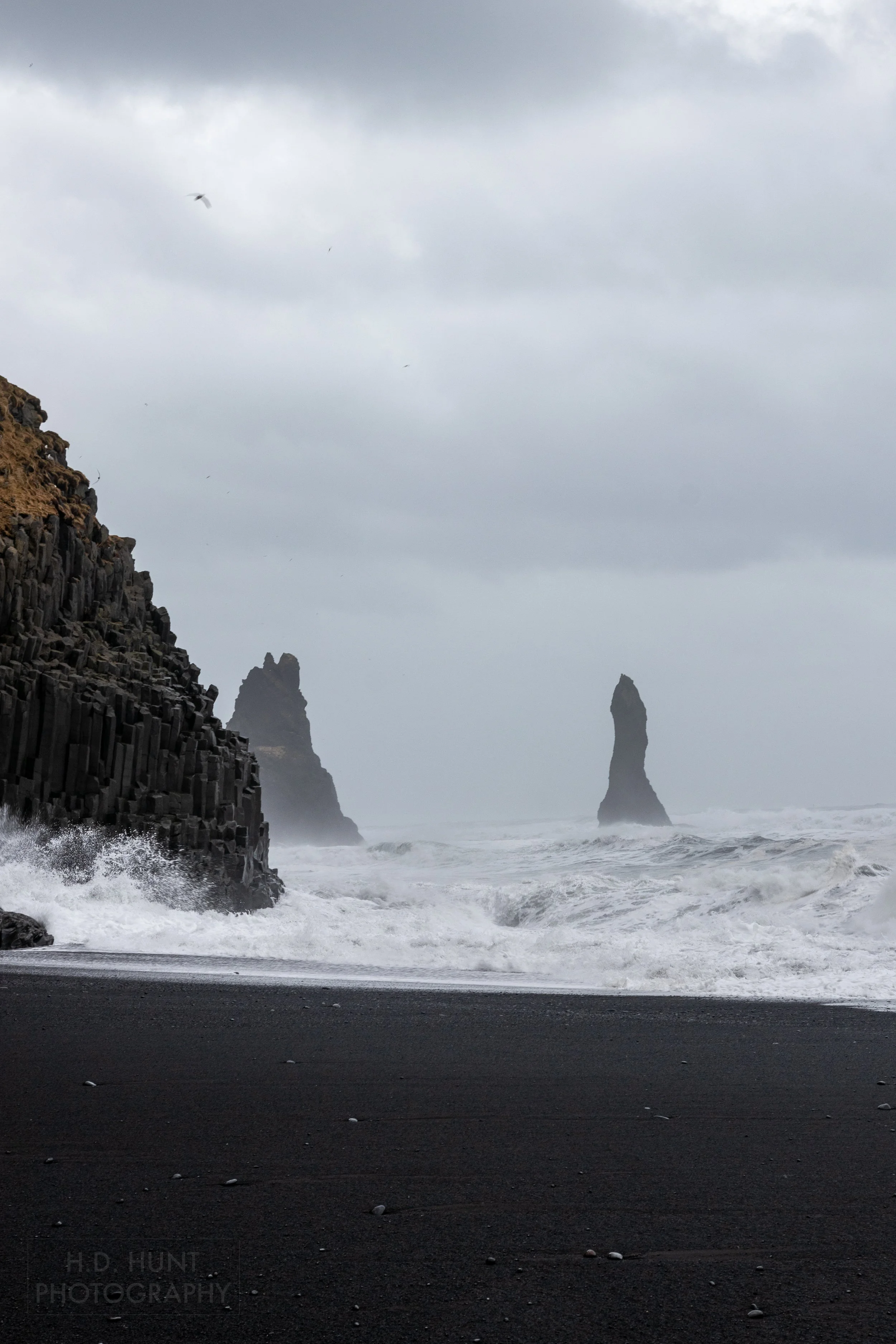 Large swells crash against stone cliff columns of basalt at Reynisfjara, Iceland